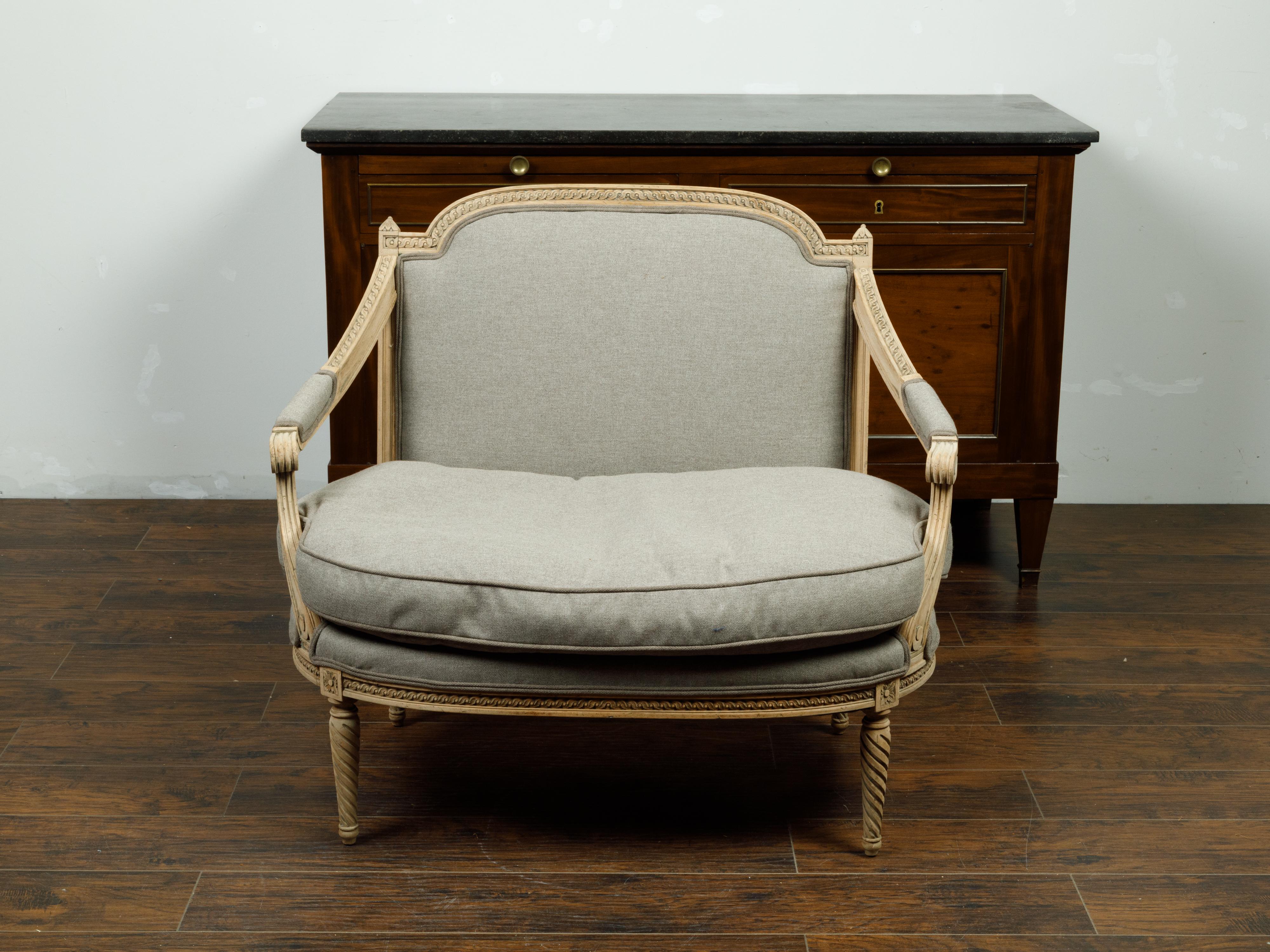 A French Louis XVI style bleached walnut marquise armchair from the 19th century, with carved guilloche frieze and new upholstery. Created in France during the 19th century, this walnut marquise (a wide bergère) features a large back carved with