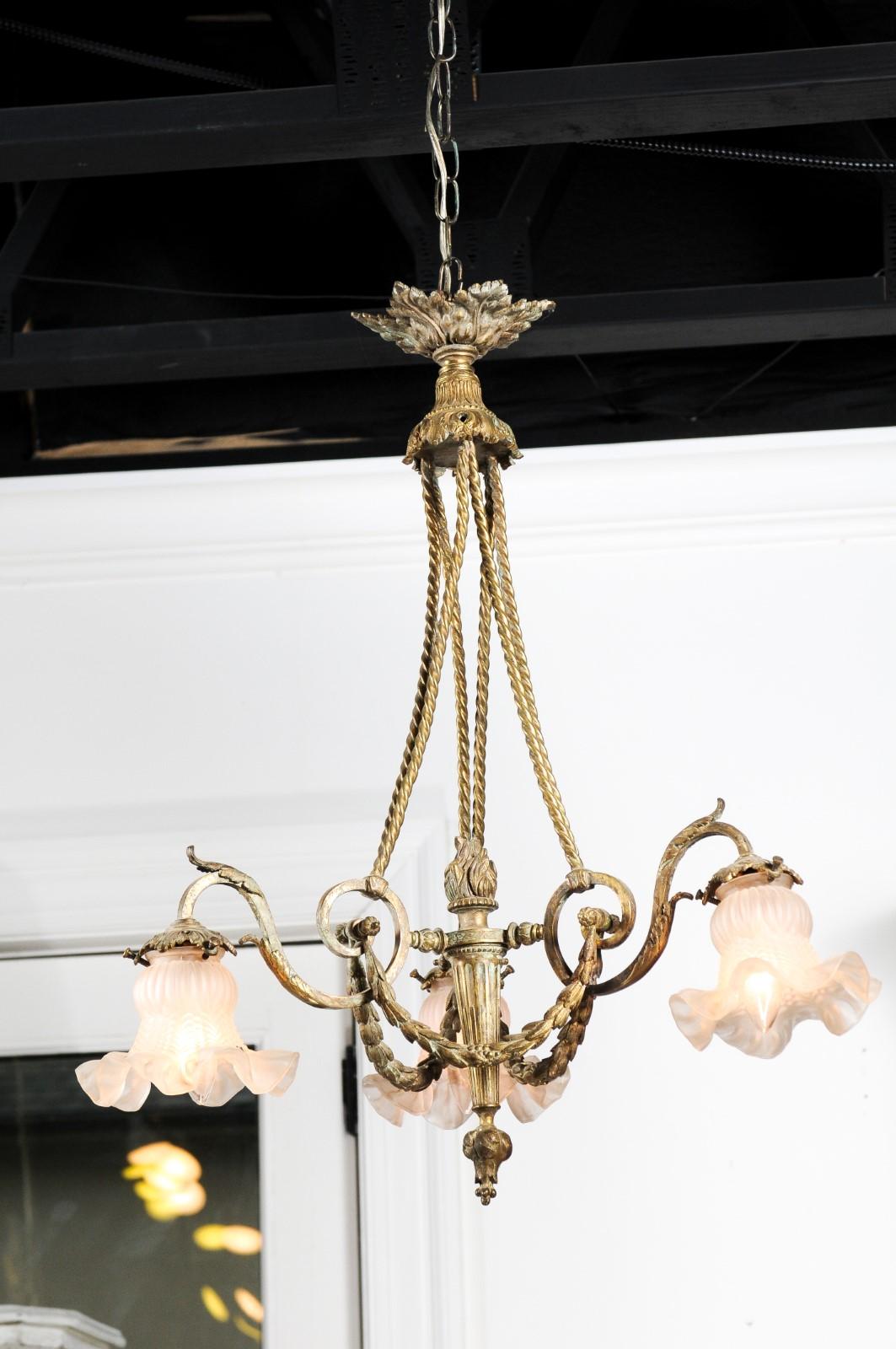 A French Louis XVI style three-light bronze chandelier from the 19th century, with flaming torch, scrolling arms, garlands and floral-shaped shades. Born in France during the 19th century, this Louis XVI style bronze chandelier features a foliate