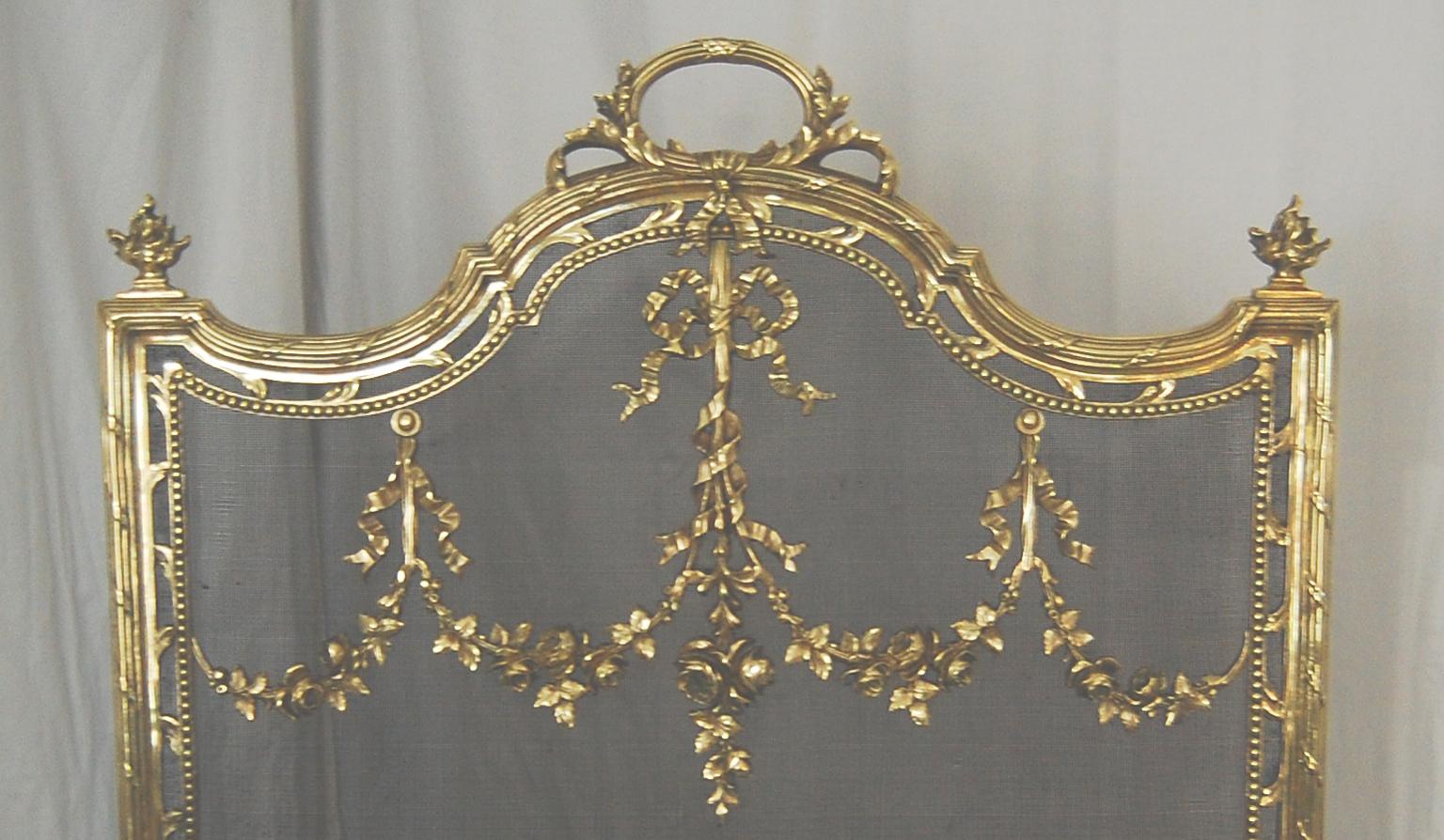  French Louis XVI style 19th century cast brass with steel mesh classic fire screen.  This heavy quality cast brass screen is adorned with floral and ribbon swags that drape over the fine steel mesh.  The integral top handle is framed by  classic