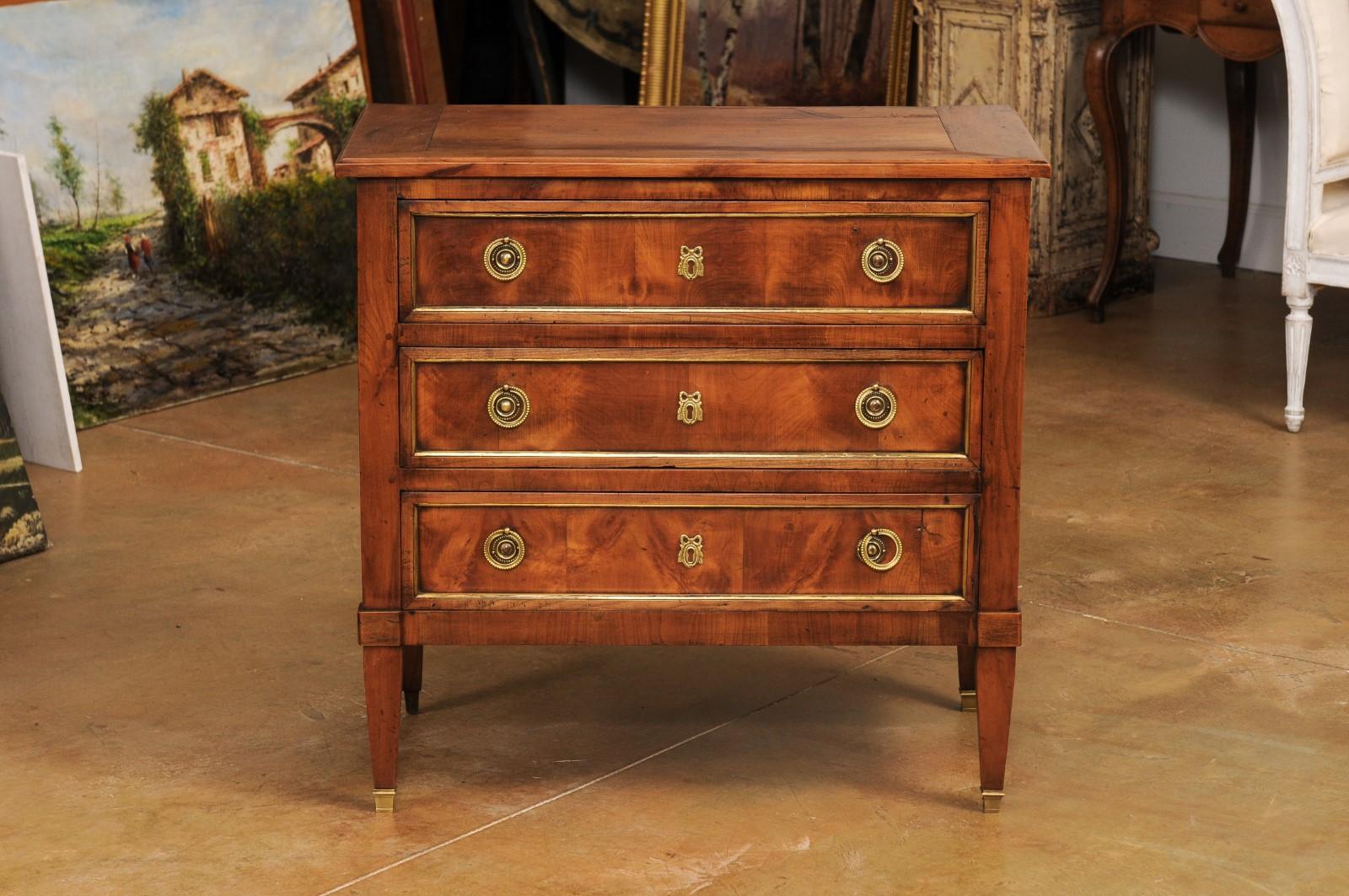 A French Louis XVI style cherry commode from the 19th century, with three drawers, brass hardware, ribbon tied escutcheons and tapered legs. Created in France during the 19th century, this cherry commode showcases the stylistic characteristics of