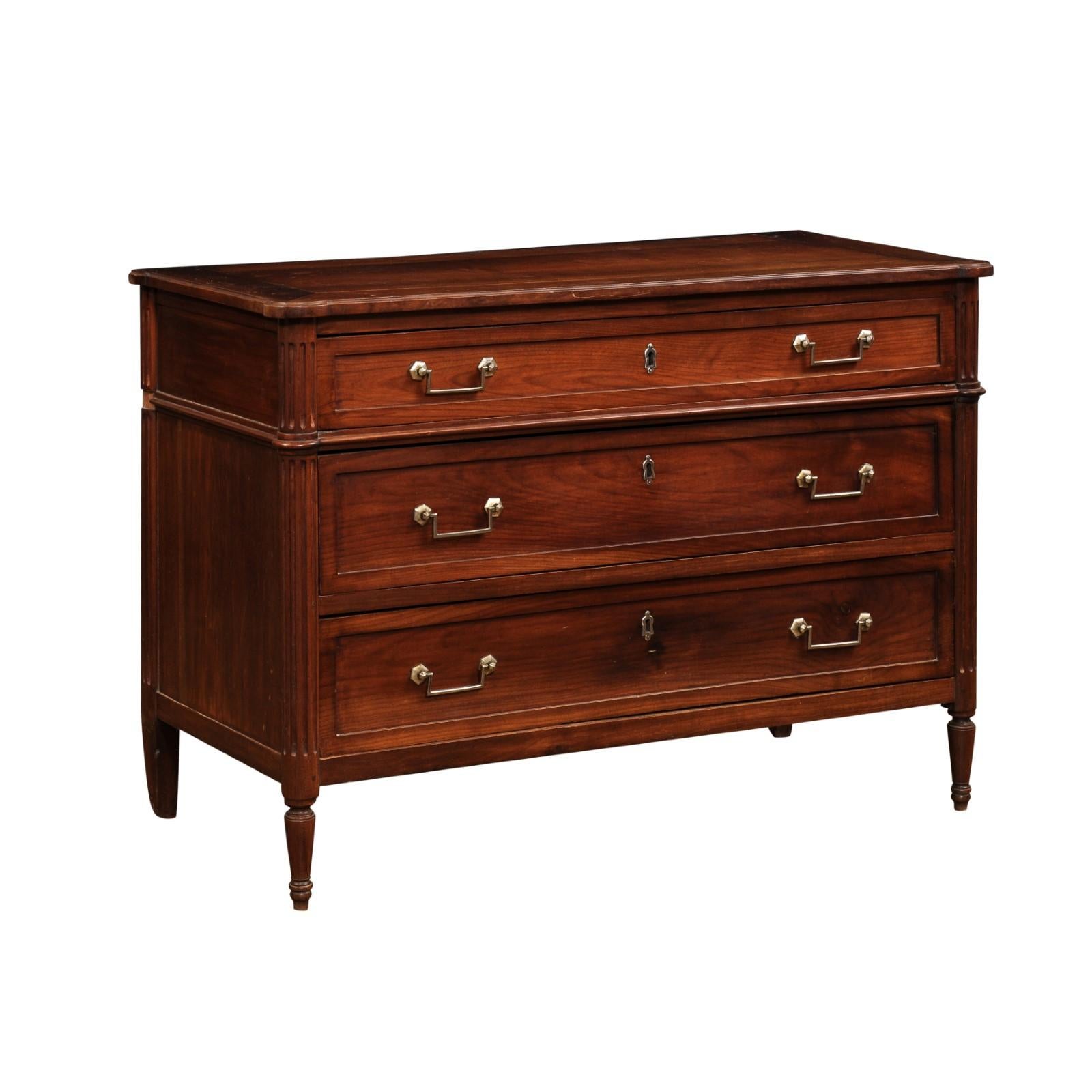 A French Louis XVI style cherry commode from the 19th century, with three graduated drawers, linear brass hardware, fluted side posts and cylindrical tapered legs. Created in France during the 19th century, this cherry commode showcases the