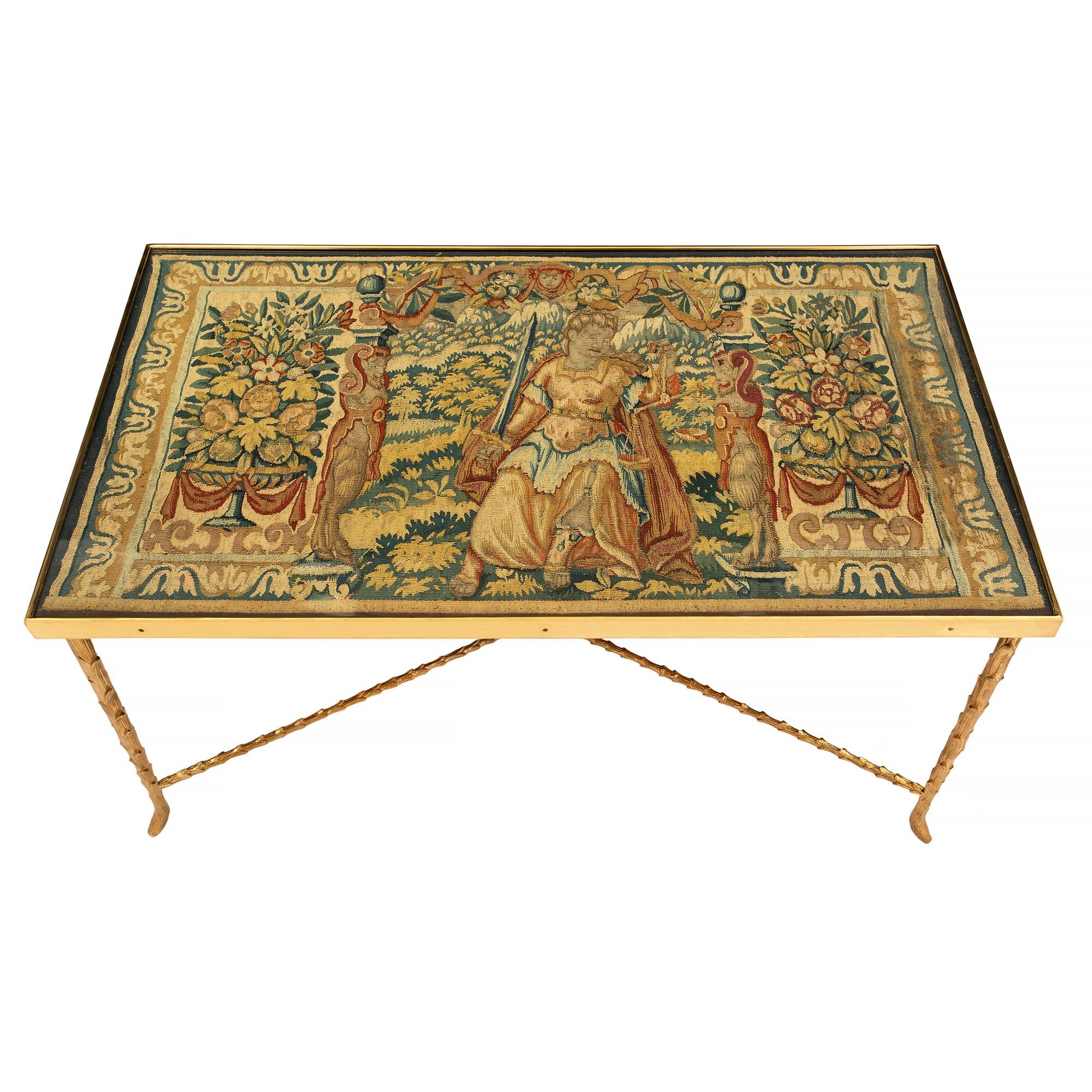 An elegant and wonderfully decorative French Louis XVI style late 19th century ormolu coffee table with an 18th century tapestry fitted top. The rectangular shaped ormolu table is raised by four foliate designed legs. The legs are joined by an 'X'