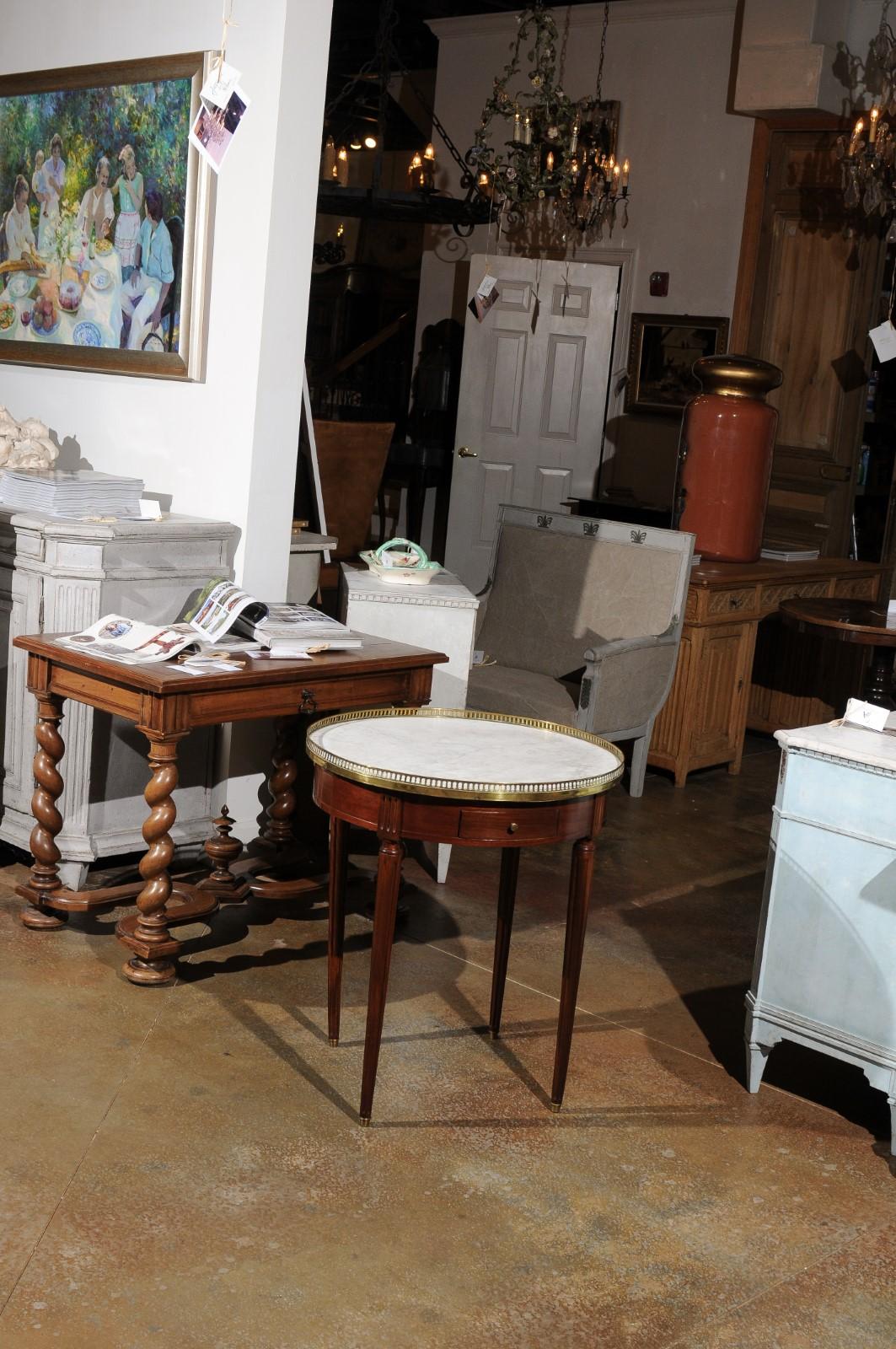 A French Louis XVI style mahogany bouillotte table from the 19th century with marble top, brass gallery, drawers and fluted legs. Born in France during the 19th century, this elegant bouillotte table features a white veined marble top surrounded by