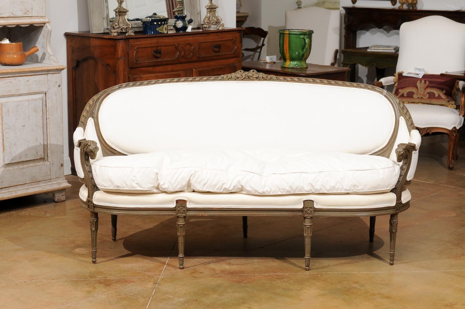 A French Louis XVI style painted wood canapé en corbeille from the 19th century, with carved rams' heads, twisted ribbons and new upholstery. Created in France during the 19th century, this sofa features a wraparound back with twisted ribbon on the