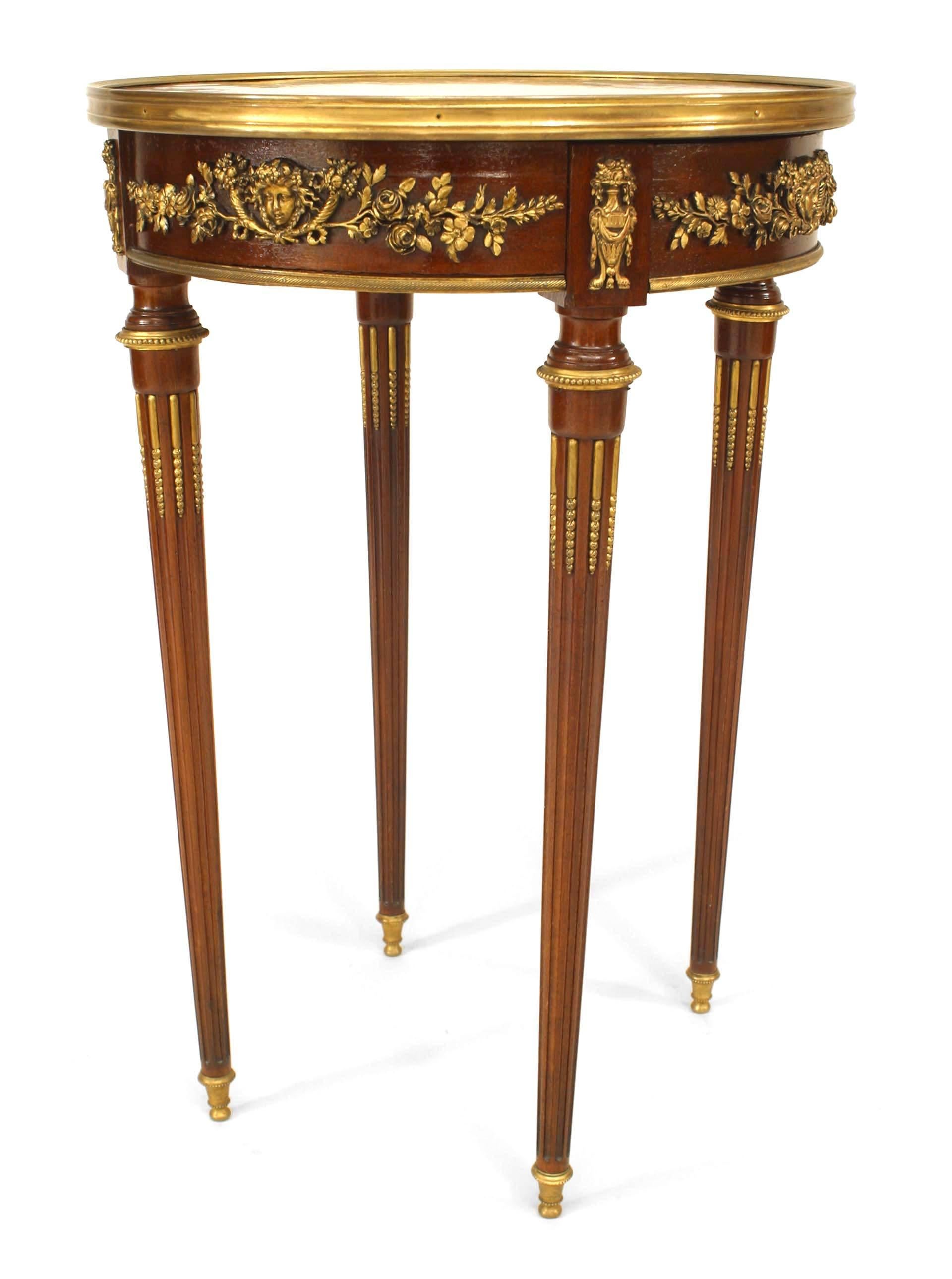 French Louis XVI-style (19th Century) round mahogany end table with bronze floral design trim on apron and legs with a parquetry inlaid top having a brass rim and a single drawer.
