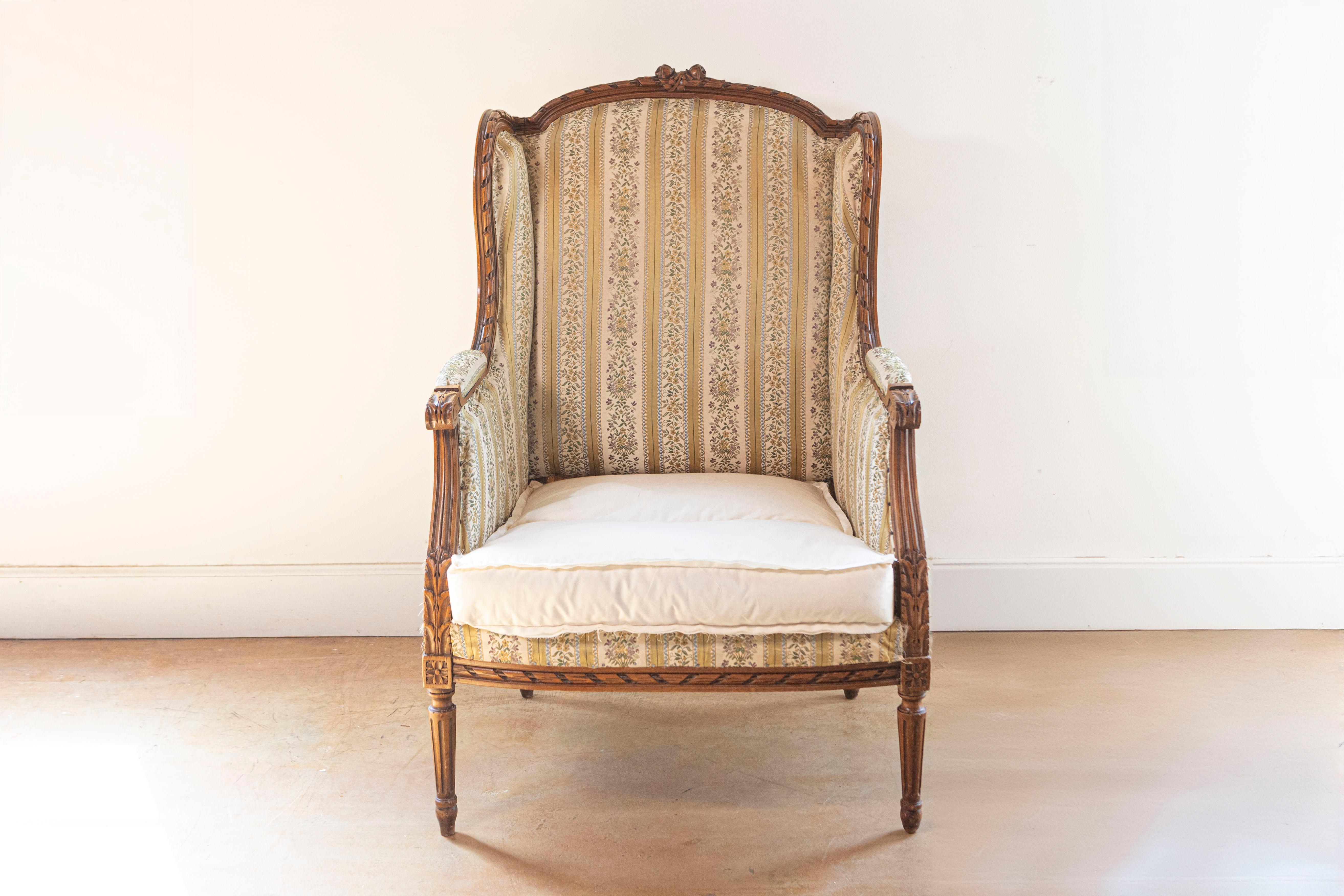 A French Louis XVI style walnut bergère wingback armchair from the 19th century with carved twisted ribbon, roses and foliage motifs. This French Louis XVI style walnut bergère wingback armchair, hailing from the 19th century, is a true testament to