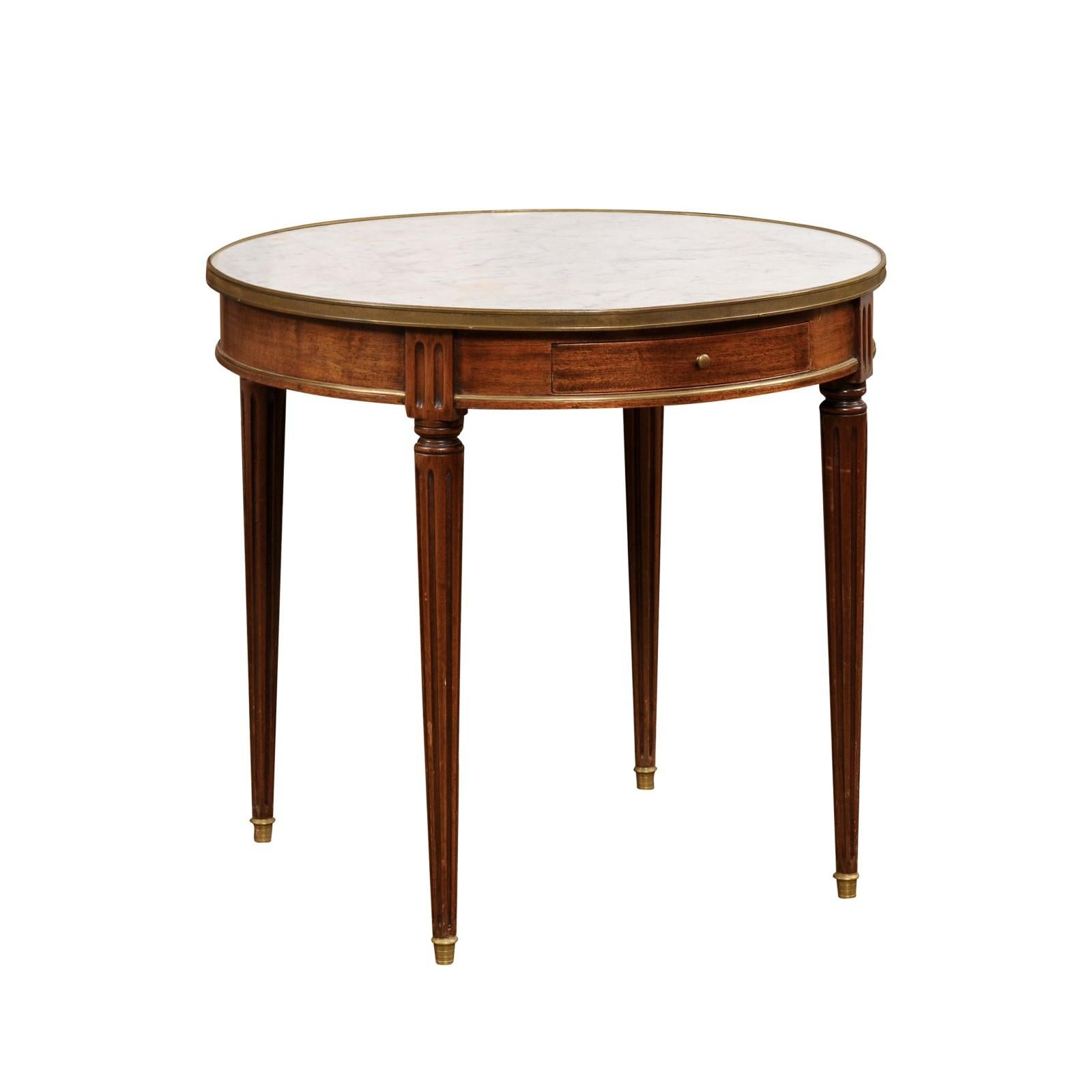 A French Louis XVI style walnut bouillotte table from the 19th century with white marble top, brass accents, single drawer and fluted legs. Created in France during the 19th century, this elegant walnut bouillotte table features a circular white