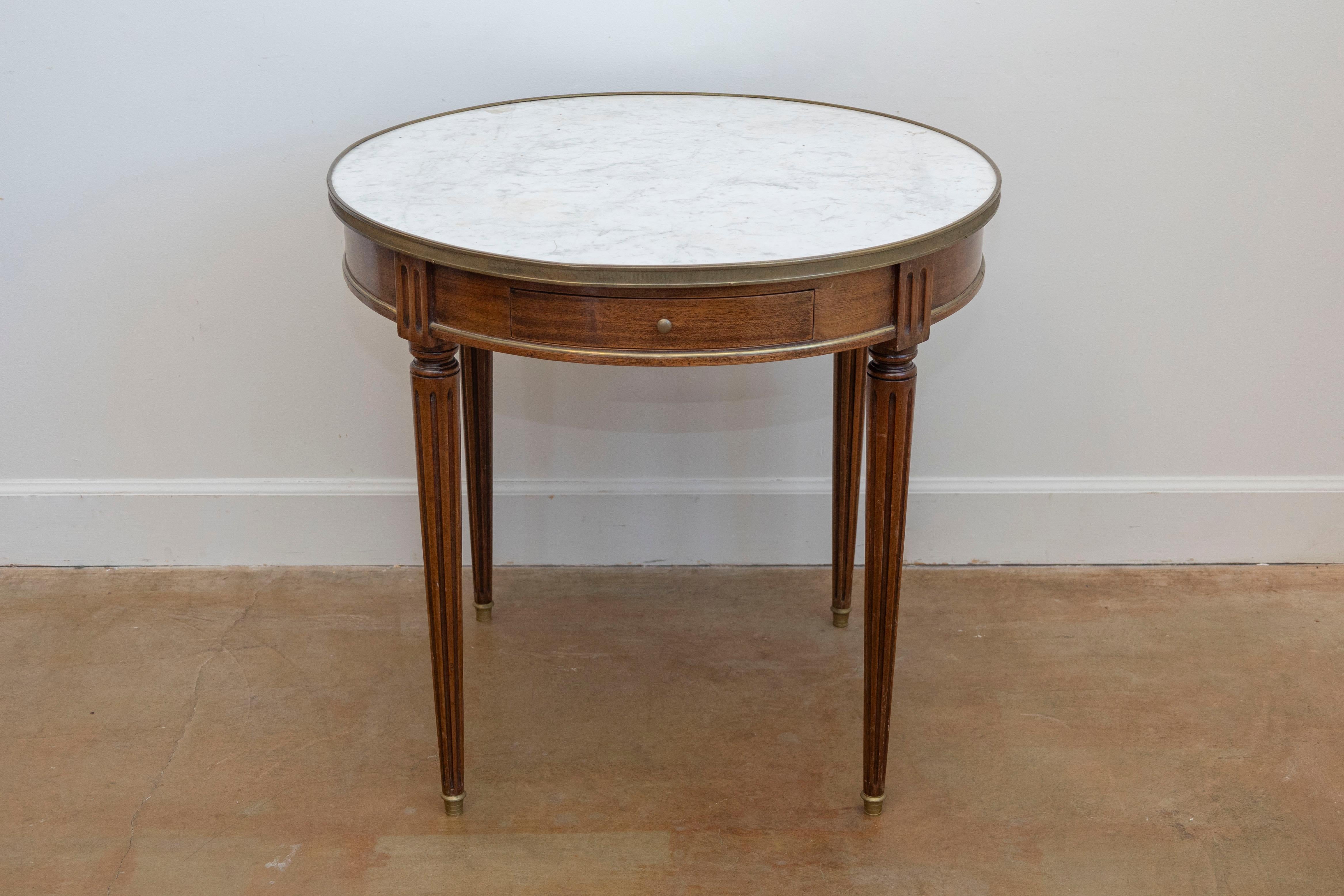 Mesa bouillotte francesa de nogal del siglo XIX, estilo Luis XVI, con tapa de mármol blanco, detalles de latón, un solo cajón y patas estriadas. Creada en Francia durante el siglo XIX, esta elegante mesa bouillotte de nogal presenta un tablero