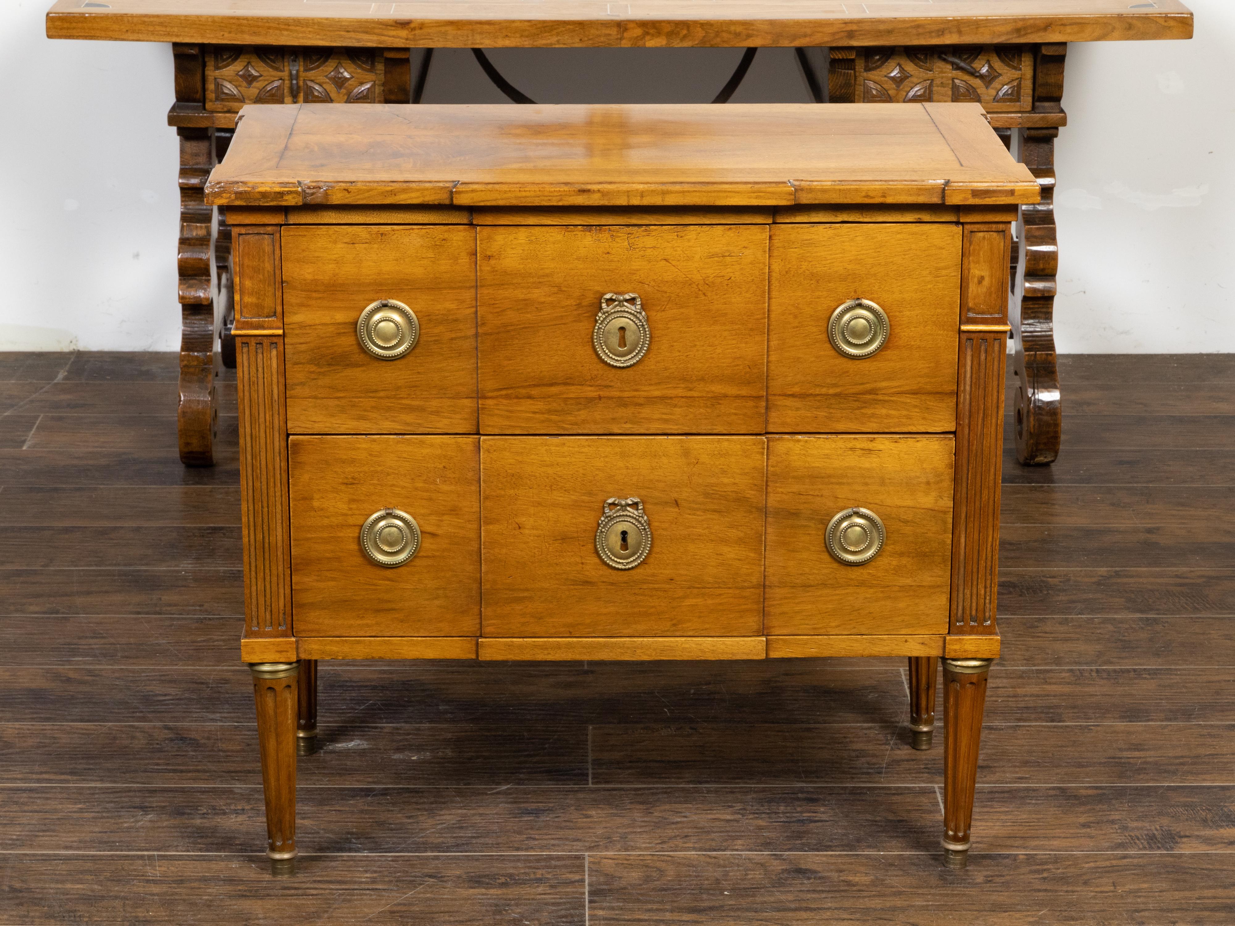 A French Louis XVI style breakfront walnut commode from the 19th century, with two drawers, fluted pilasters, tapered cylindrical legs and brass hardware. Created in France during the 19th century, this walnut commode features a rectangular top with