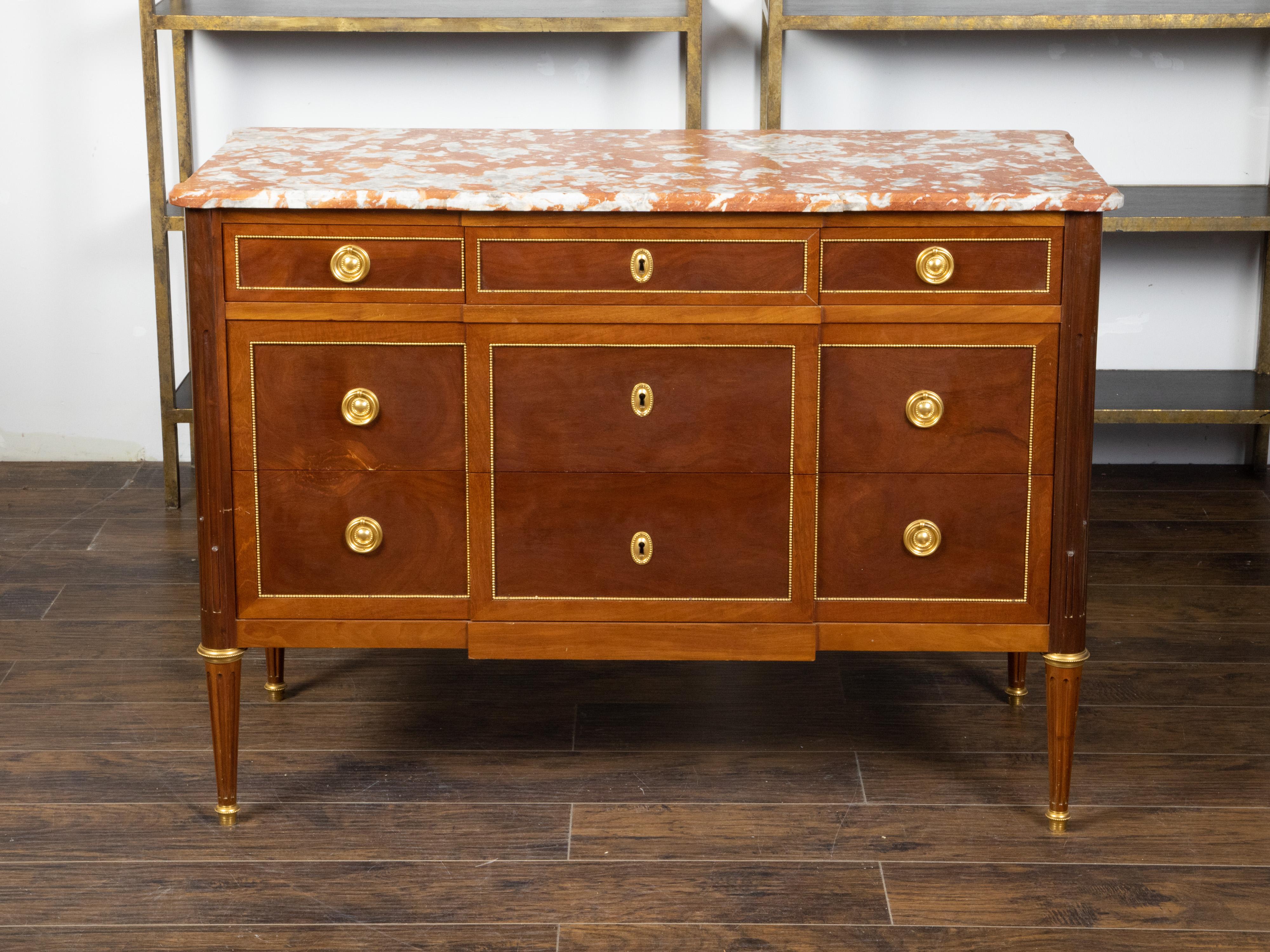 A French Louis XVI style walnut commode from the 19th century, with red marble top, gilt bronze accents and drawers. Created in France during the 19th century, this walnut commode features a rectangular red marble top with rounded corners, sitting