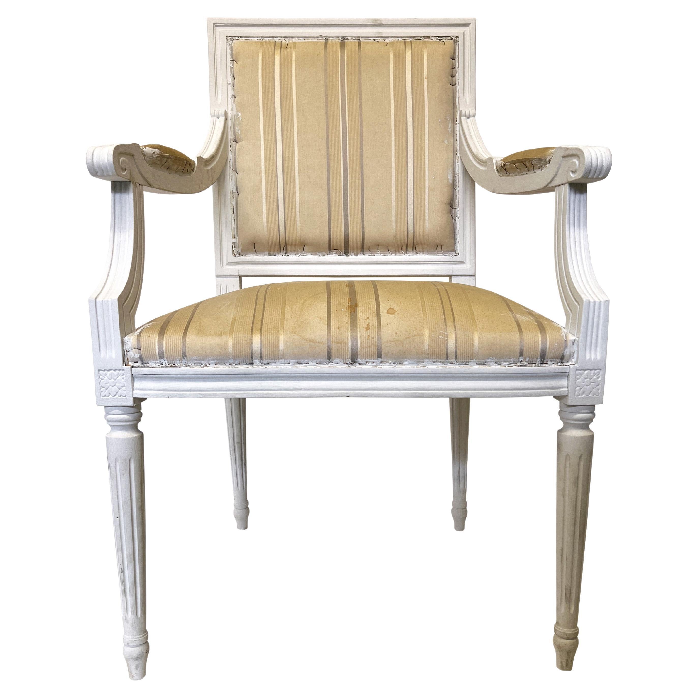 These French Louis XVI style armchairs or dining chairs have an elegant silhouette and a carved wooden frame upholstered in a striped fabric. The chair has a square backrest and seat carved with classicizing details. The white painted armchairs are