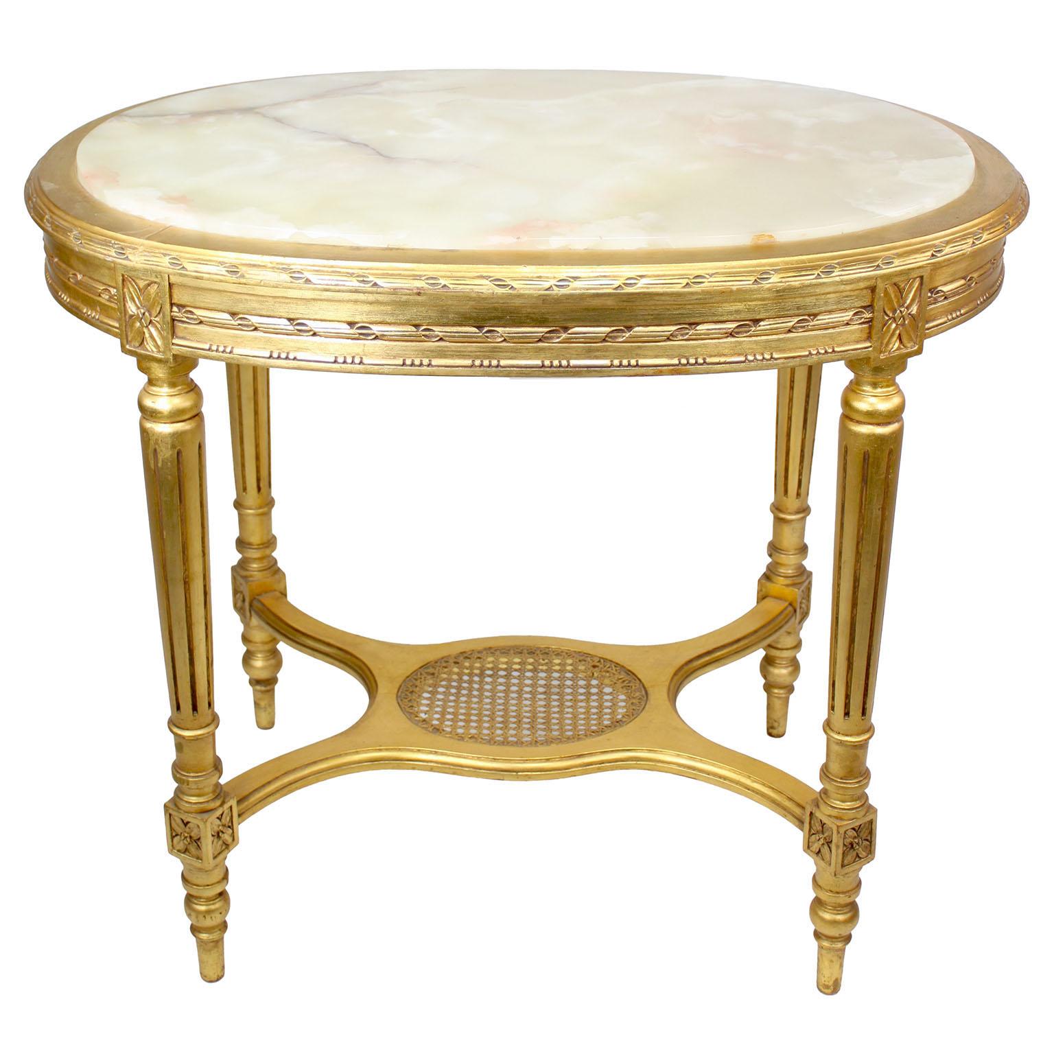 A French Louis XVI Style 'Belle Époque' Oval Giltwood Carved Center Table with Onyx Top. The decorated carved apron fitted with a veined light-green onyx top and raised on four fluted tapered legs conjoined with a 