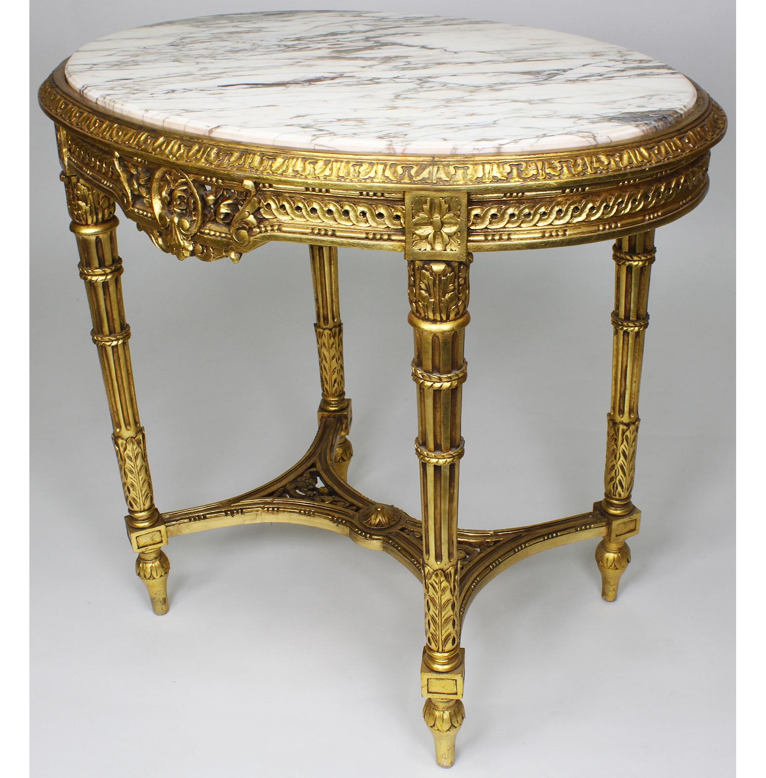 Ovaler, geschnitzter Mitteltisch aus Goldholz mit Marmorplatte im französischen Louis XVI-Stil. Die kunstvoll verzierte Schürze ist mit einer geäderten weißen Marmorplatte versehen und steht auf vier kannelierten Beinen, die mit einer geschnitzten