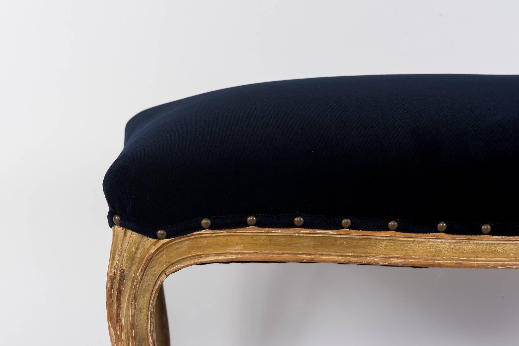 A 1920s French Louis XVI style giltwood bench newly upholstered in a navy velvet with nailhead detail.