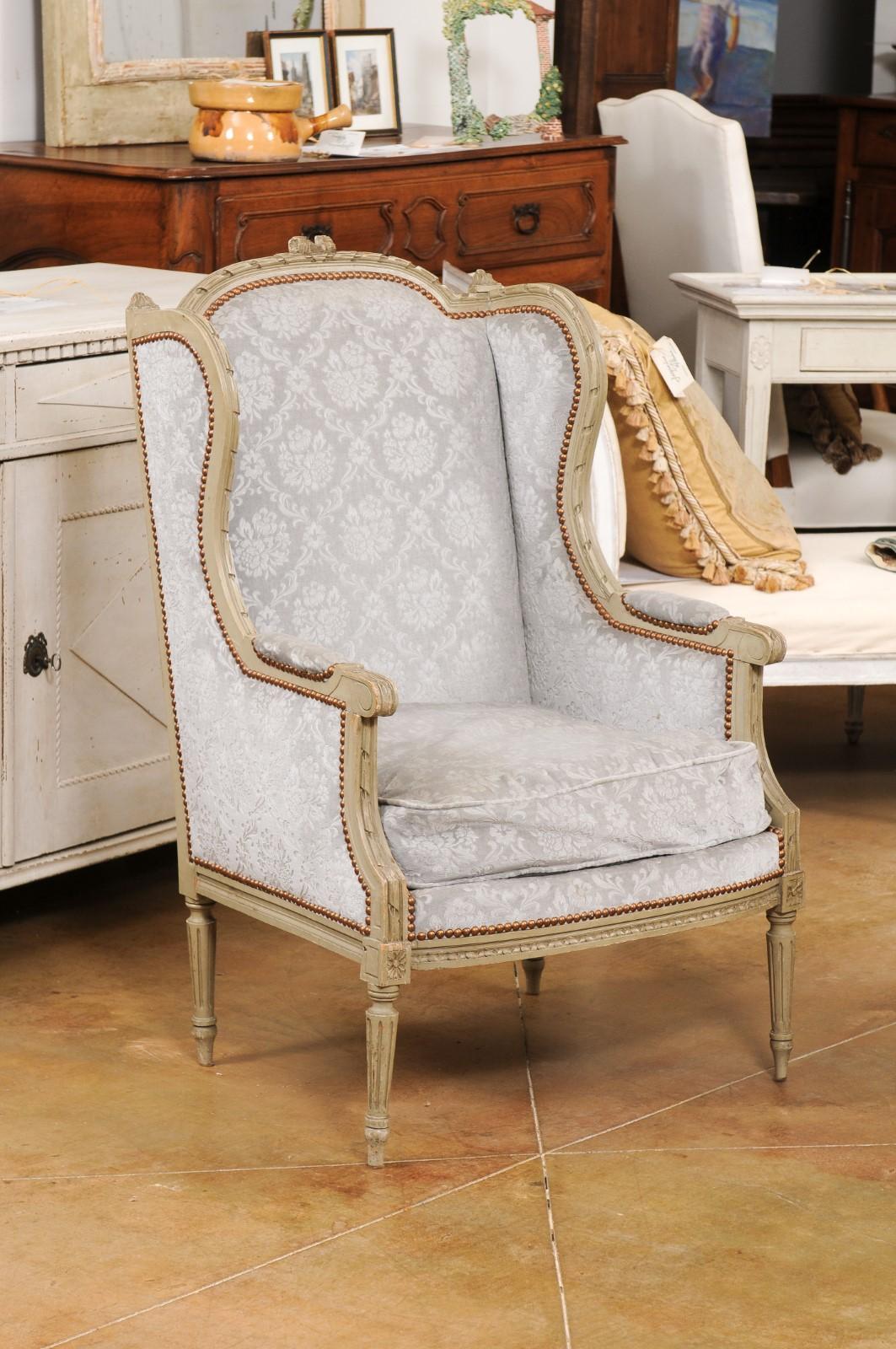 A pair of French Louis XVI style painted wood wingback bergères à oreilles from the early 20th century, with carved ribbons, twisted rails, scrolling knuckles, fluted legs and floral upholstery. Created in France during the Turn of the Century which
