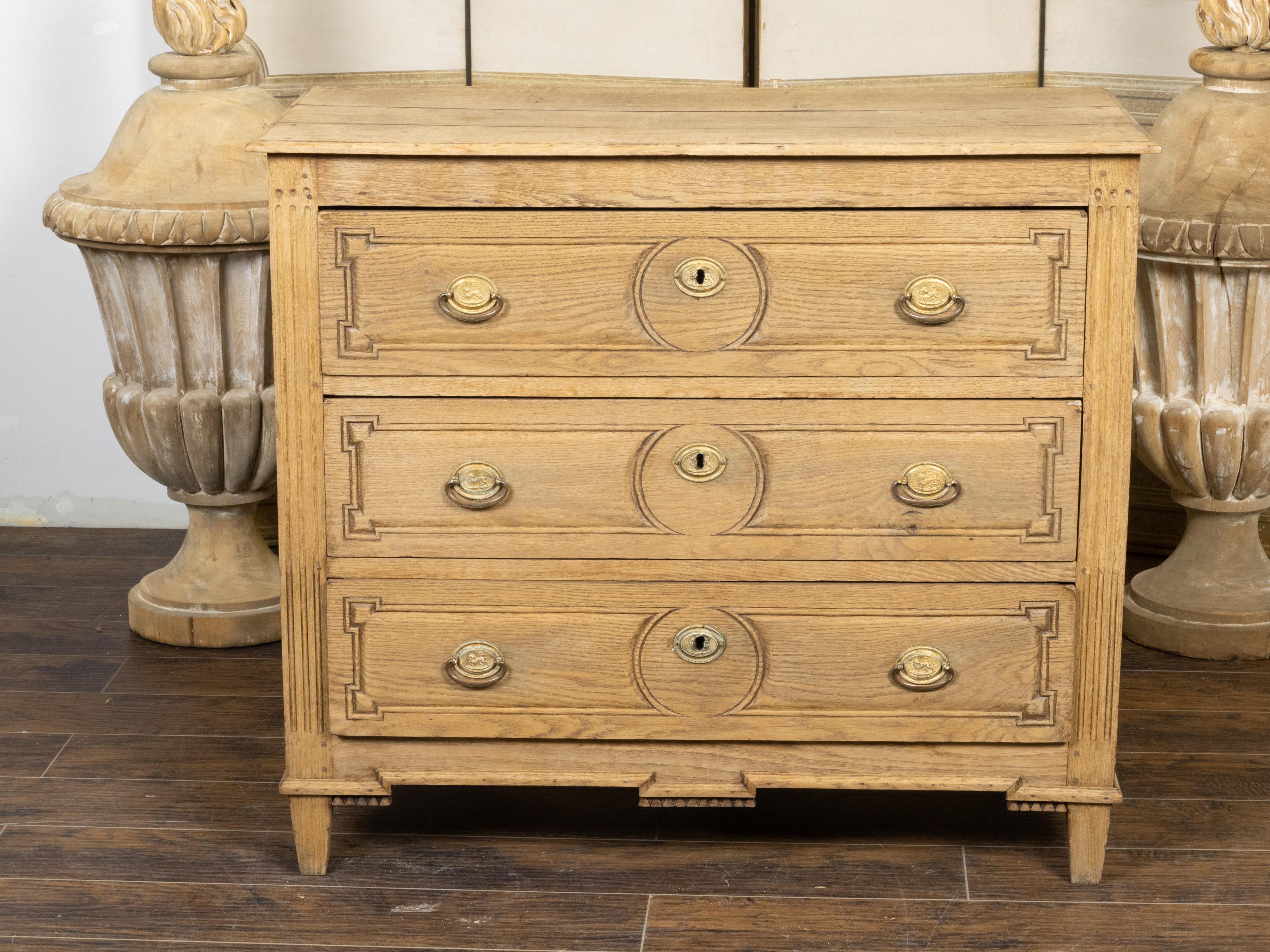 A French Louis XVI style bleached oak chest from the 19th century, with three drawers, carved panels, brass hardware and fluted side posts. Created in France during the 19th century, this bleached oak chest showcases the stylistic characteristics of