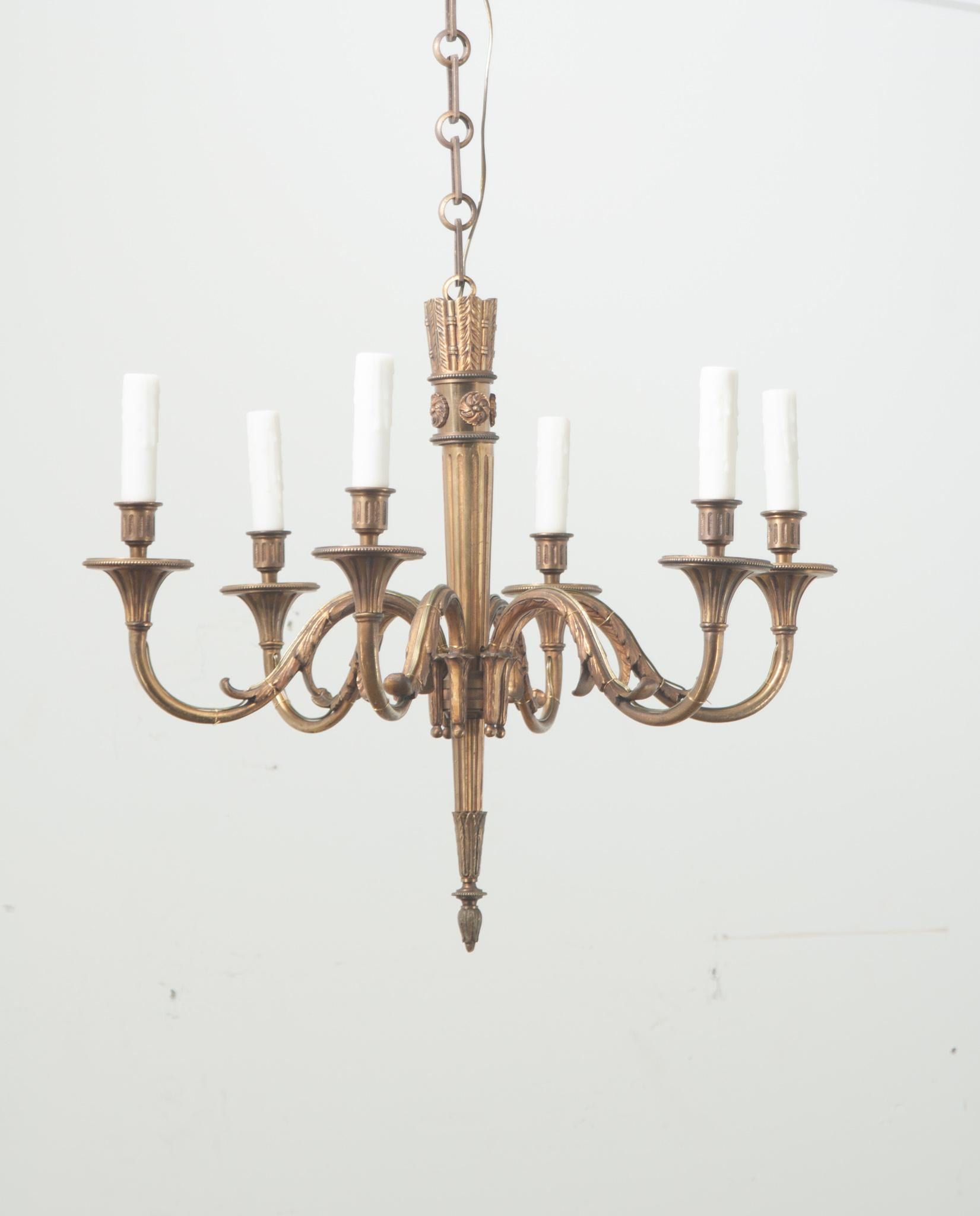 A classic Louis XVI style six light brass chandelier. The center of the fixture is shaped like a quiver of arrows and has six substantial scalloped arms with faux candle covers. This chandelier has been cleaned and wired for US electrical using UL