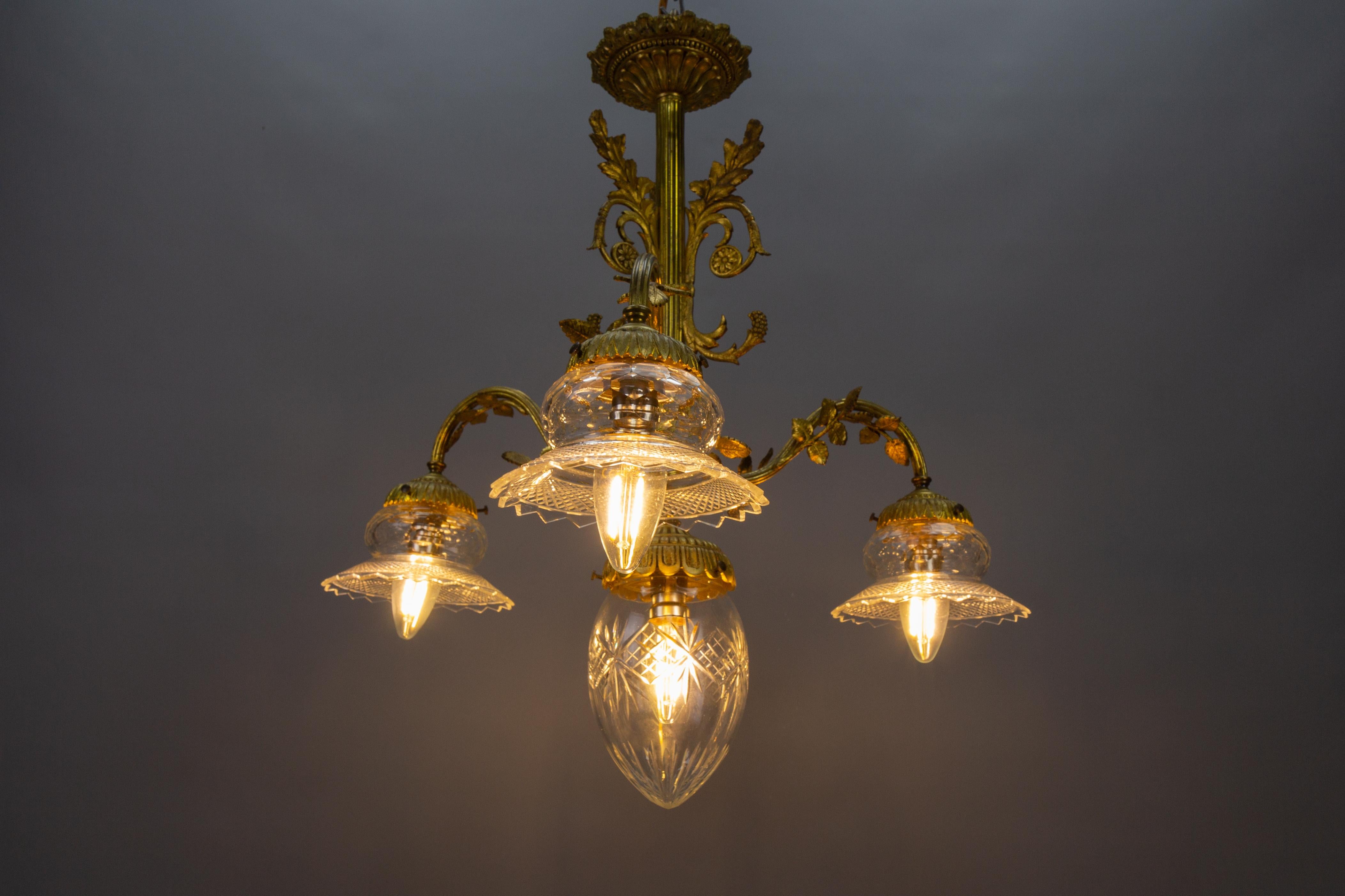 French Louis XVI style bronze and clear cut glass four-light chandelier from circa 1920s.
This adorable Neoclassical or Louis XVI-style bronze chandelier is adorned with scrolls, acanthus, and rose leaves and features three arms, each with a 