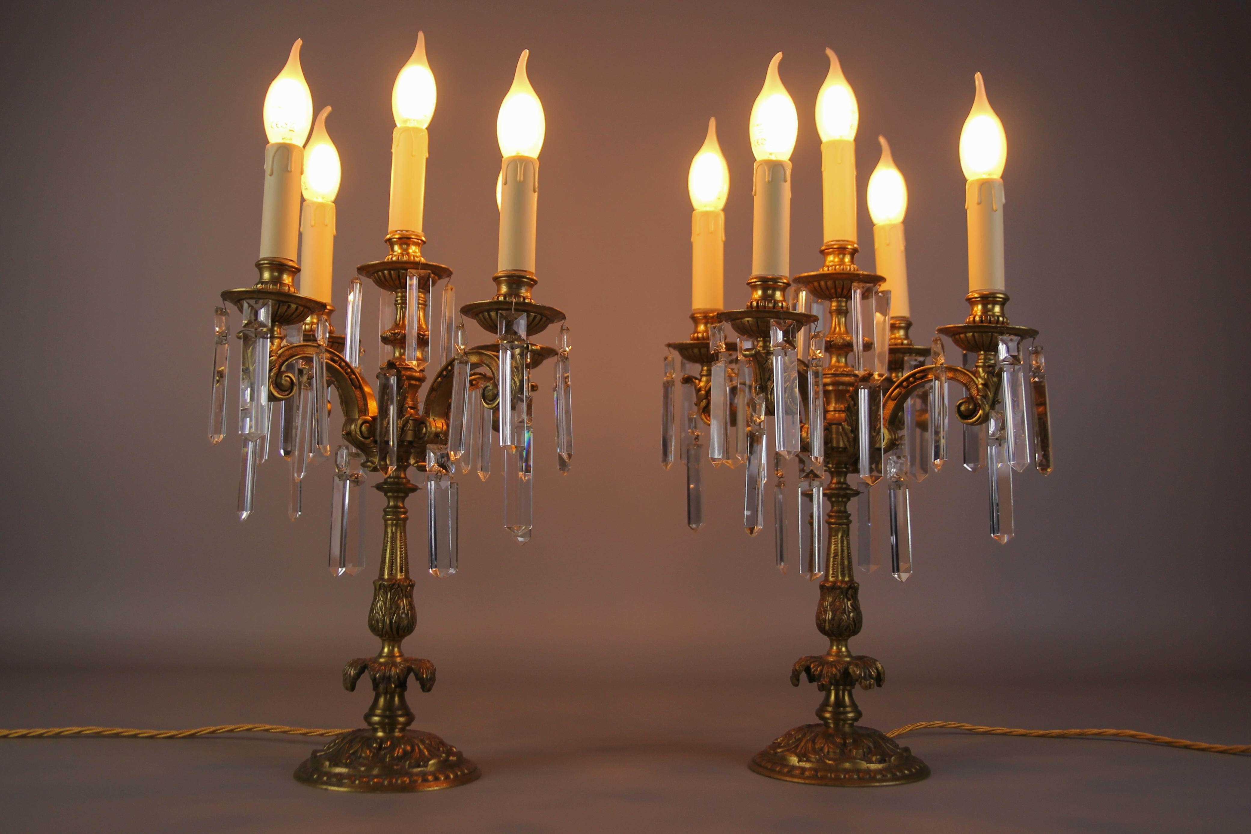 Pair of French Louis XVI style bronze and crystal candelabra table lamps. These impressive table lamps feature five bronze arms, embellished with hanging cut crystal prisms that reflect the light of elegance and glamorous beauty. Each lamp has five