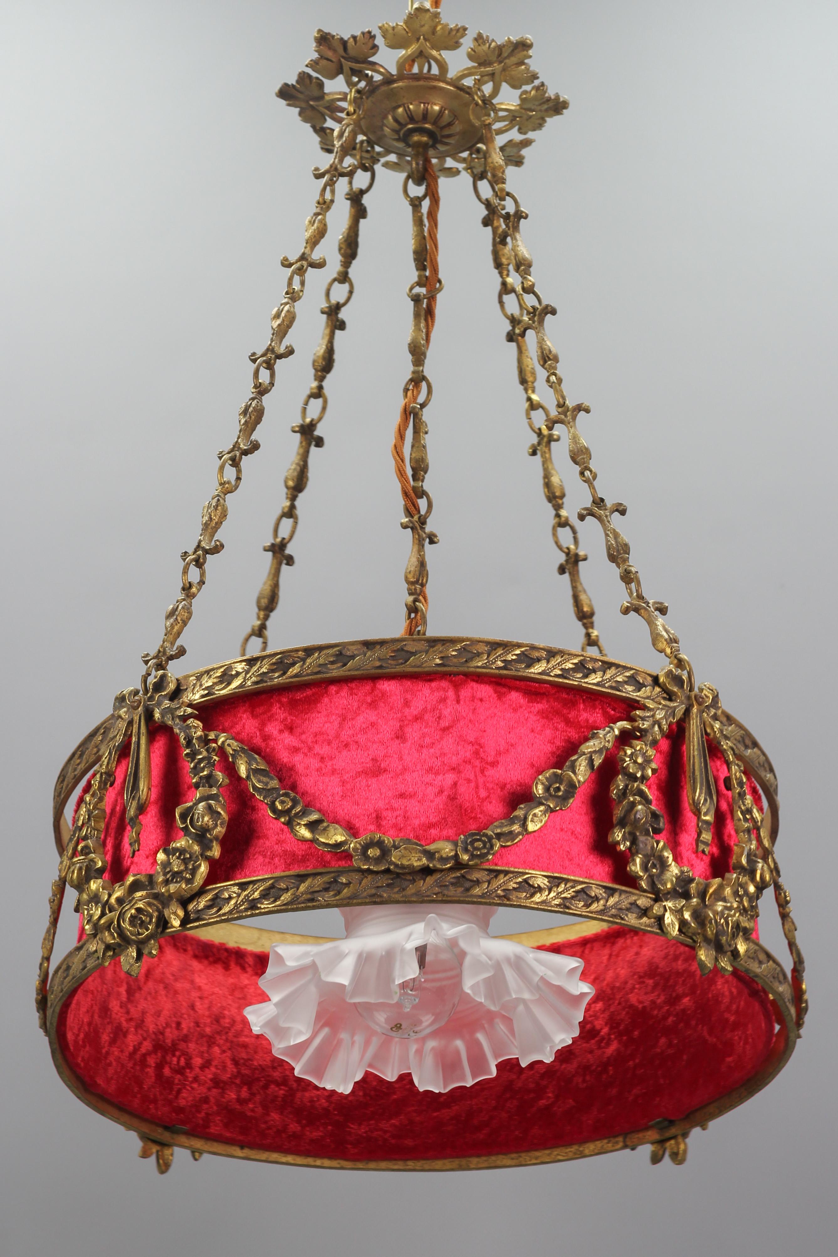 An elegant French Louis XVI style bronze chandelier with red fabric drum lampshade. This beautiful chandelier is suspended by four ornate bronze chains and features bronze floral garlands, tied with decorative bows. One central interior light -