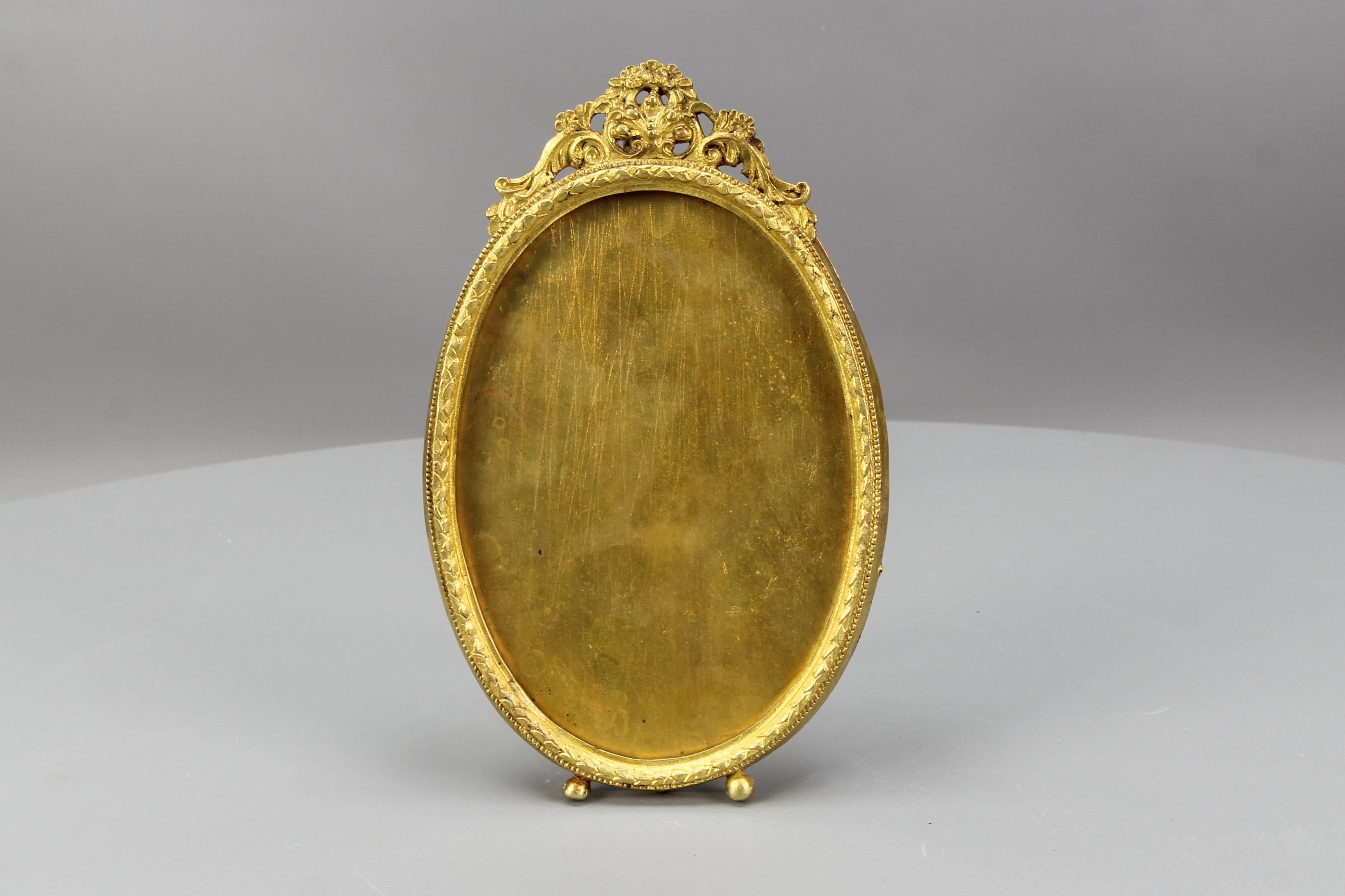 French Louis XVI style bronze oval photo or picture desktop easel frame from circa the 1900s.
This adorable picture frame is made of bronze and brass and has an easel supporting leg on the back. Decorated with flowers and leaf scrolls above the oval