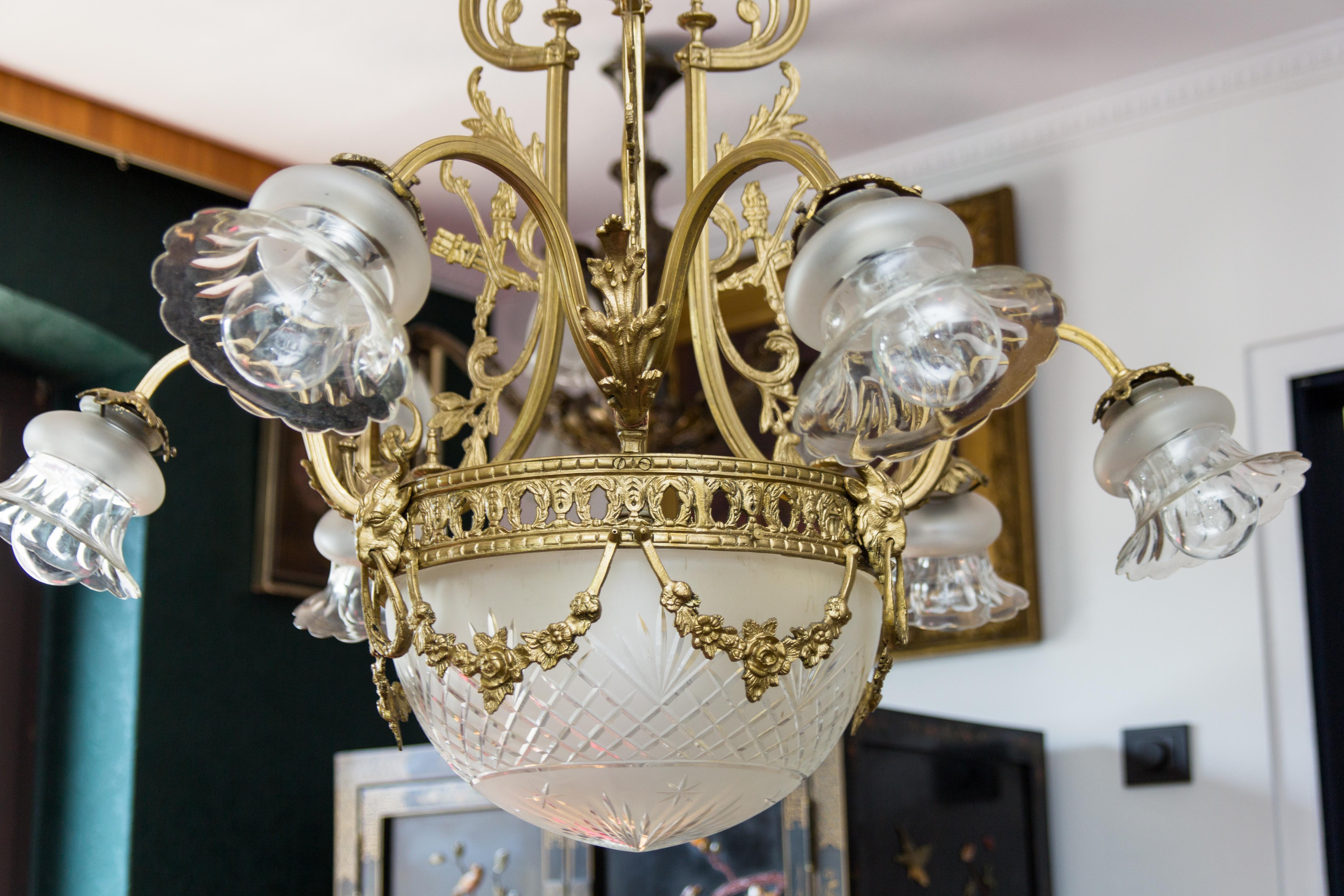 A beautiful Louis XVI-style bronze seven-light chandelier from the 1920s. Six bronze arms, each with floral shape glass lampshade, seventh light is located in the center of the cut glass lampshade, decorated with bronze flower chains held by ram