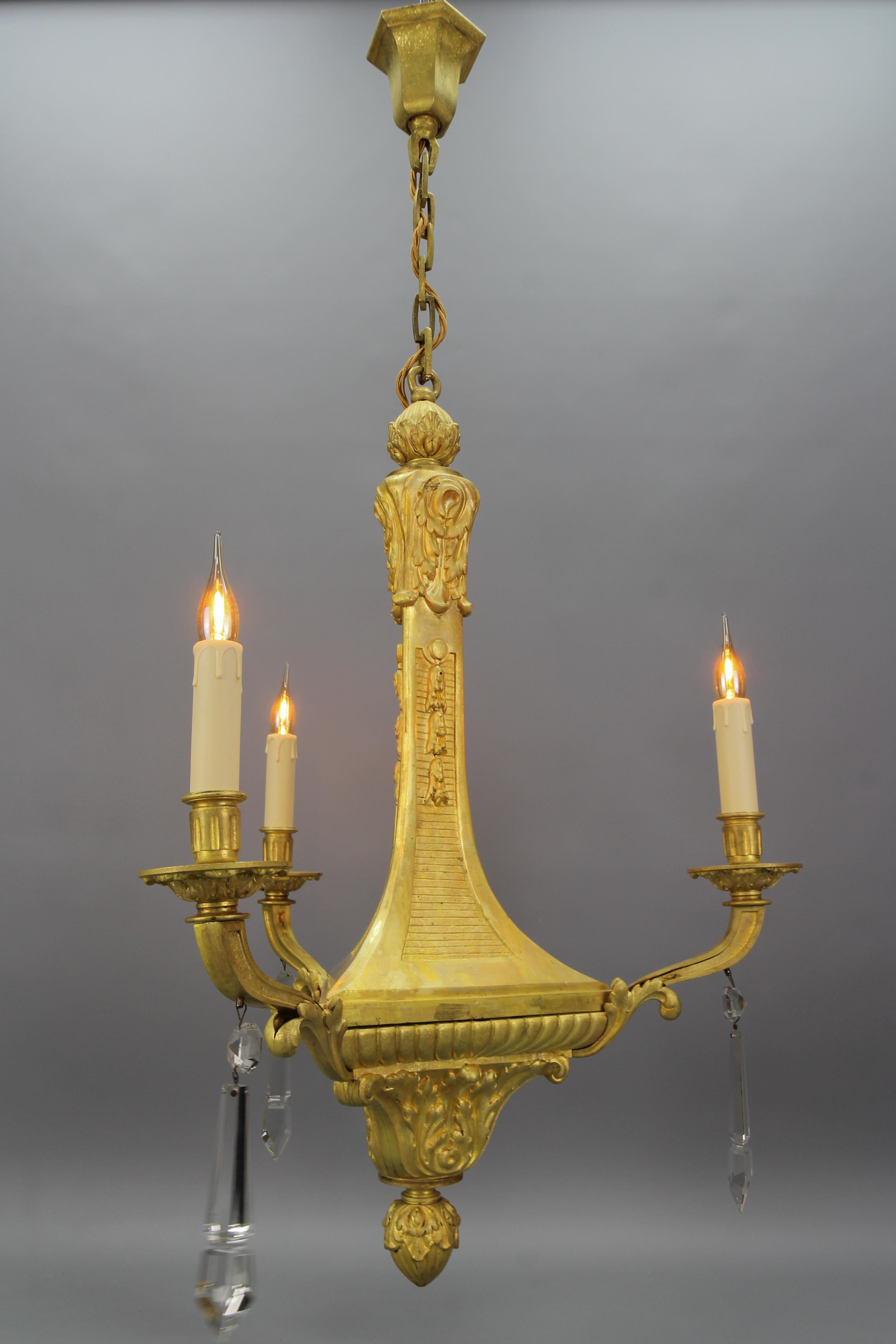 French Louis XVI style bronze and crystal three-light chandelier from the early 20th century.
This impressive and unusually shaped Louis XVI-style bronze chandelier, richly decorated with acanthus leaves, features three bronze arms, each with a