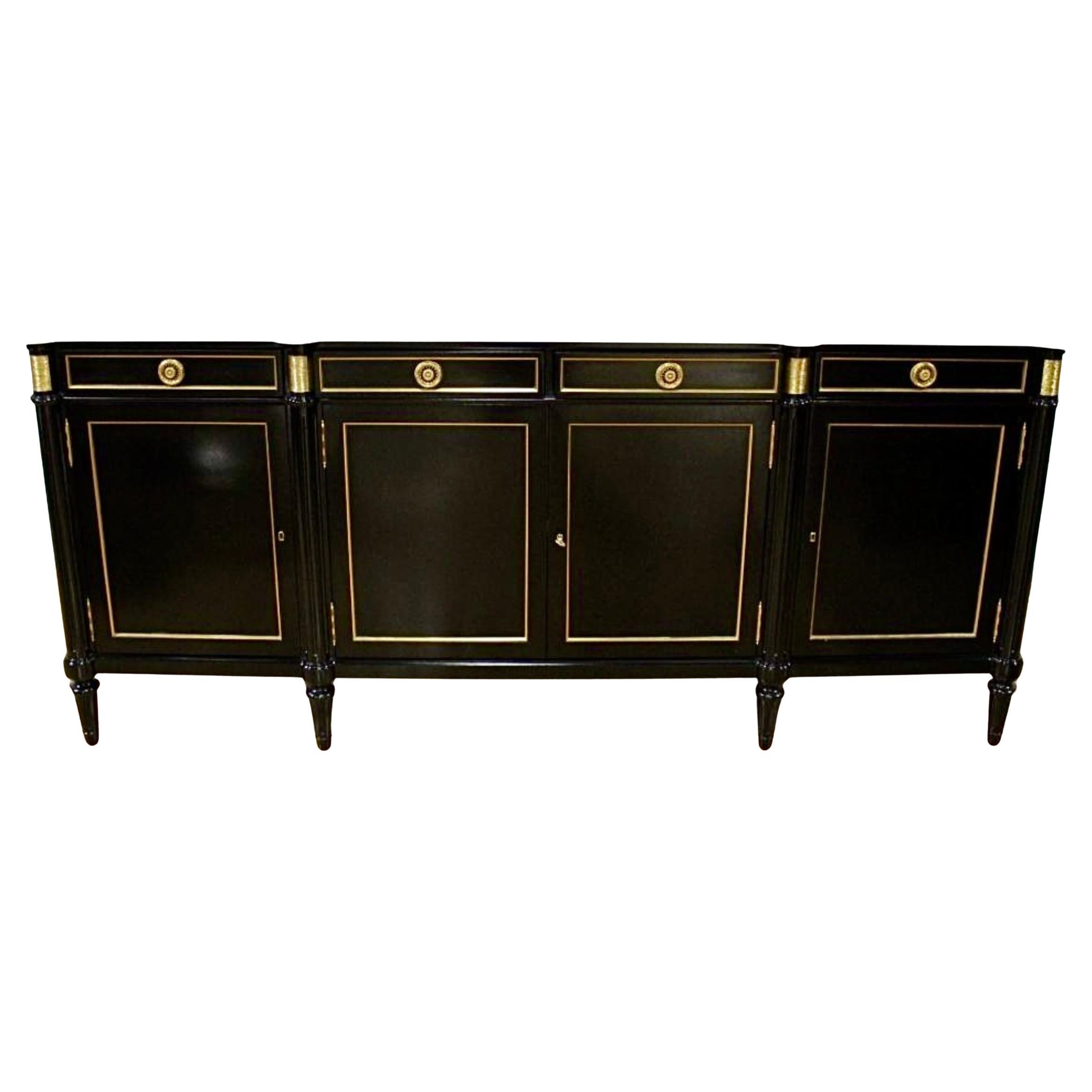 French Louis XVI Style Ebonized and Gilt Sideboard Enfilade Buffet with Carerra Marble Top. Piece features an elegant ebonized finish with refined gilt accents. The sideboard showcases four paneled doors adorned with gilt trim,  each opening to