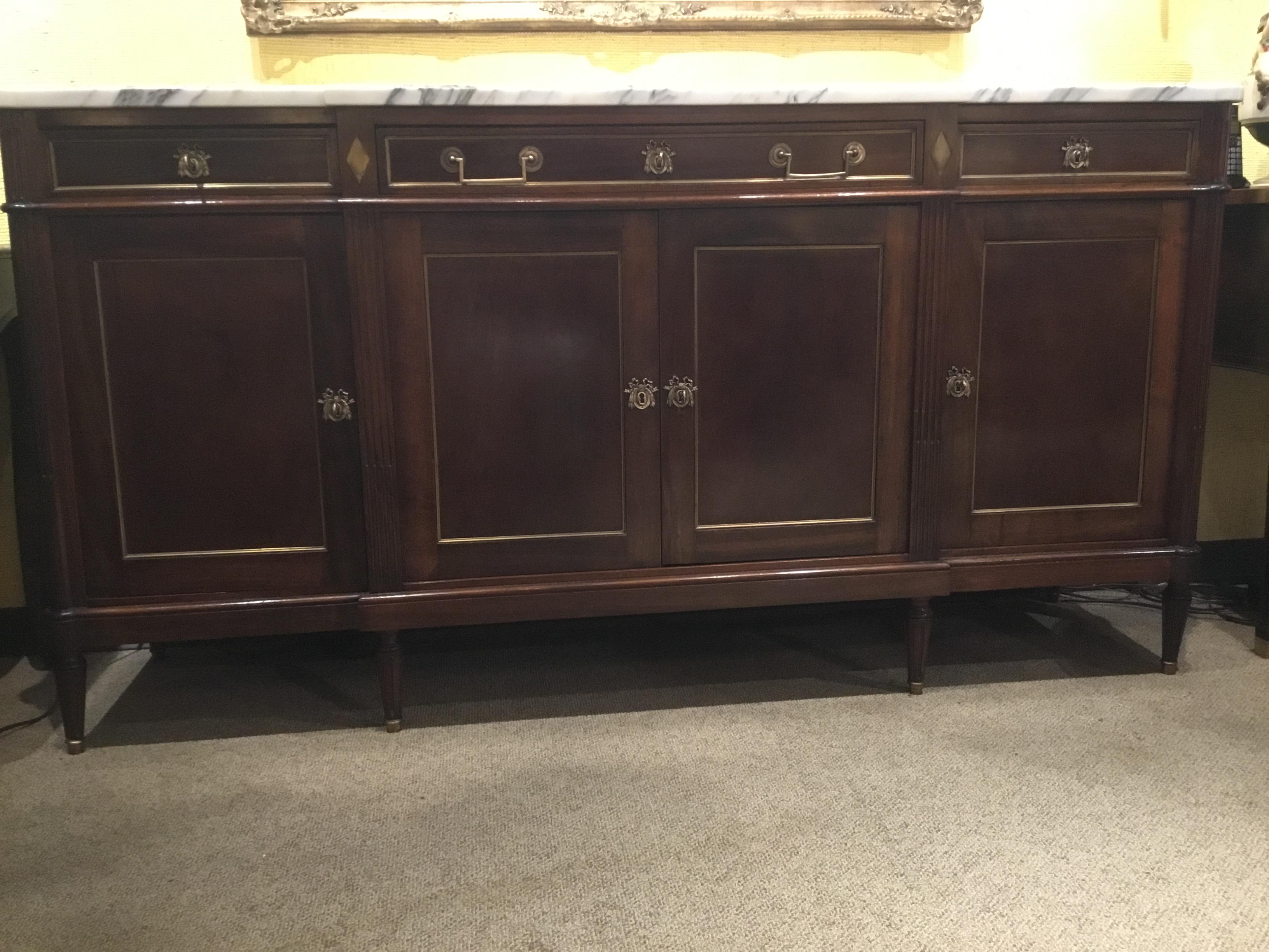 Louis XVI style buffet, marble top in white, having fluted corner posts, fitted with three
drawers, center drawer with a divided interior, over four cabinet doors, opening to an
interior shelf, rising on tapered legs, ending in gilt metal capped