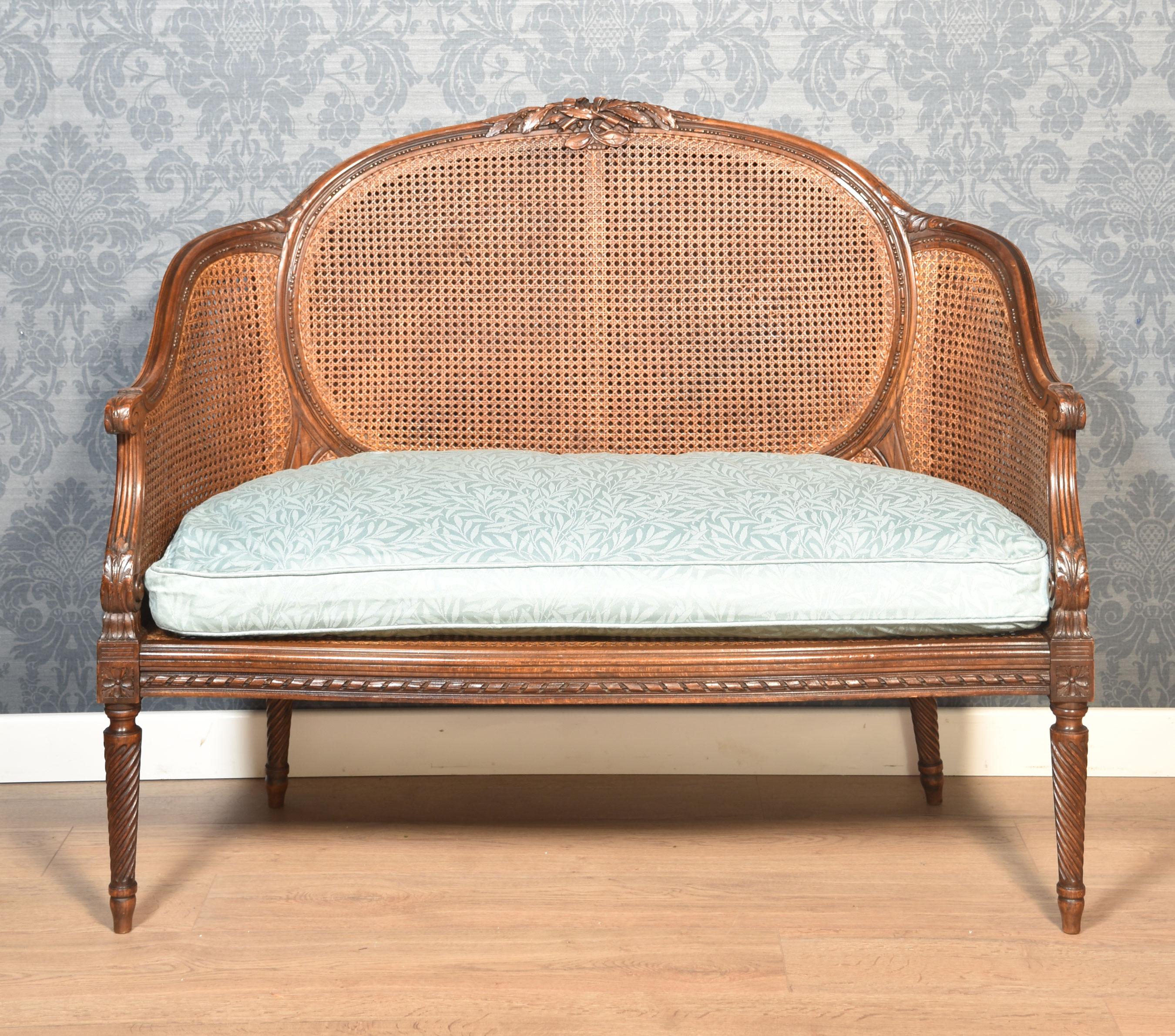 French Louis XVI style canapé settee, the carved rail in the typical manner of the period with highly detailed ribbon work along the crest among foliage, the frame a repeating motif of detailed leaves. To the scrolling acanthus caped arms, flanking