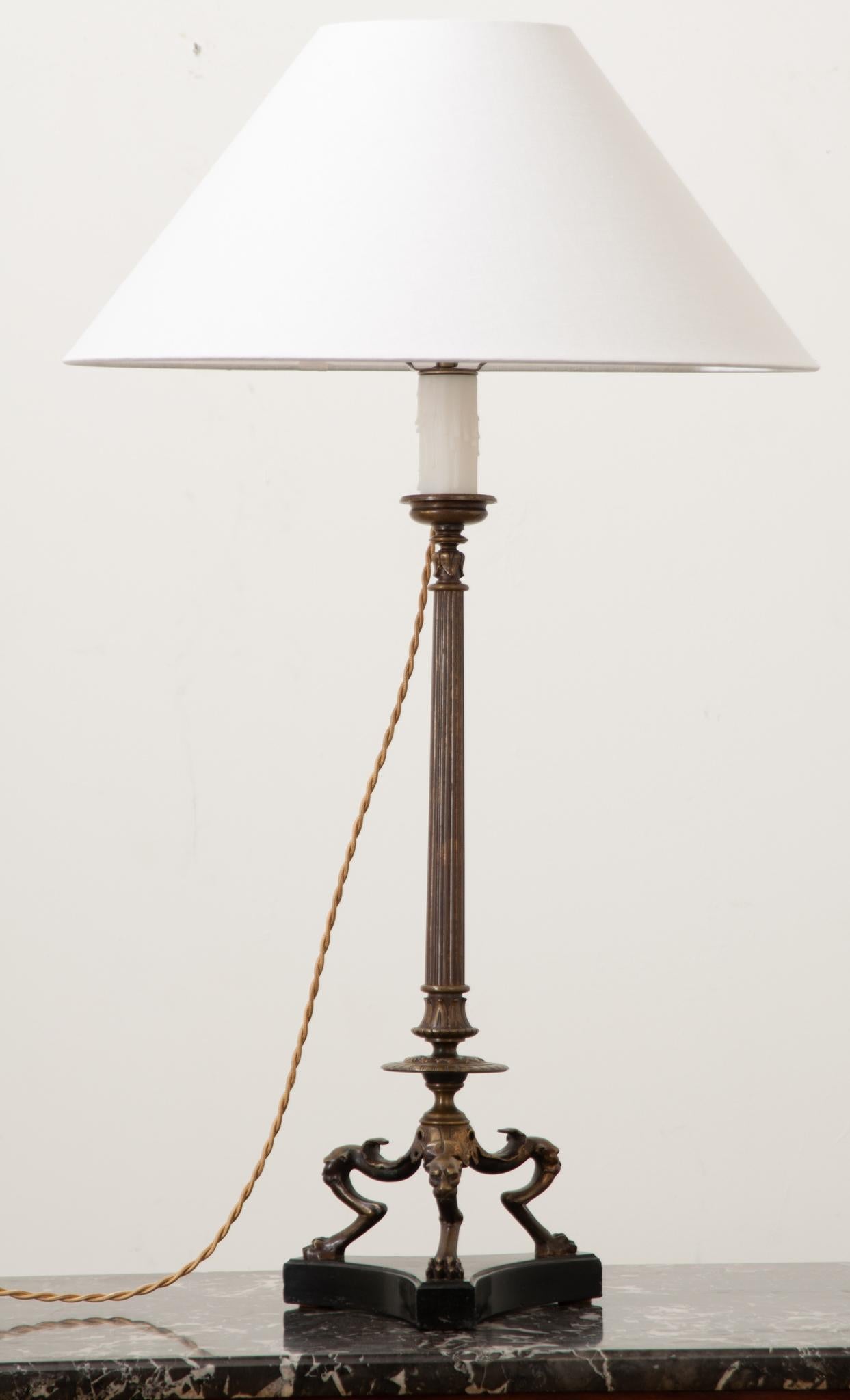 This tall Louis XVI style bronze candelabra is now an elegant table lamp. A slender fluted center column is lifted on three hind legs with paw feet over a shaped base of black marble. The lamp has recently been cleaned and wired for US electrical