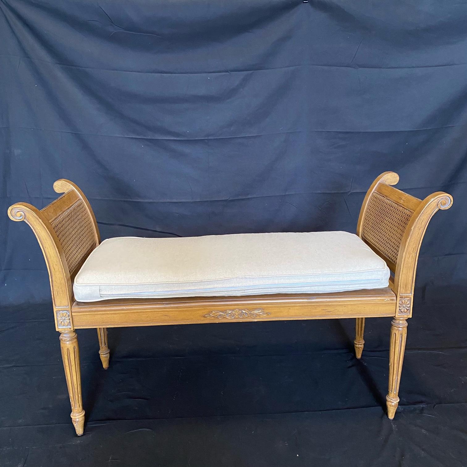 Beautiful French Louis XVI style bench having hand carved wooden frame with a painted finish and low armrest guards at either end curving down to the rectangular base. The frame has incised detailing and fluted carvings to the knee blocks raised on