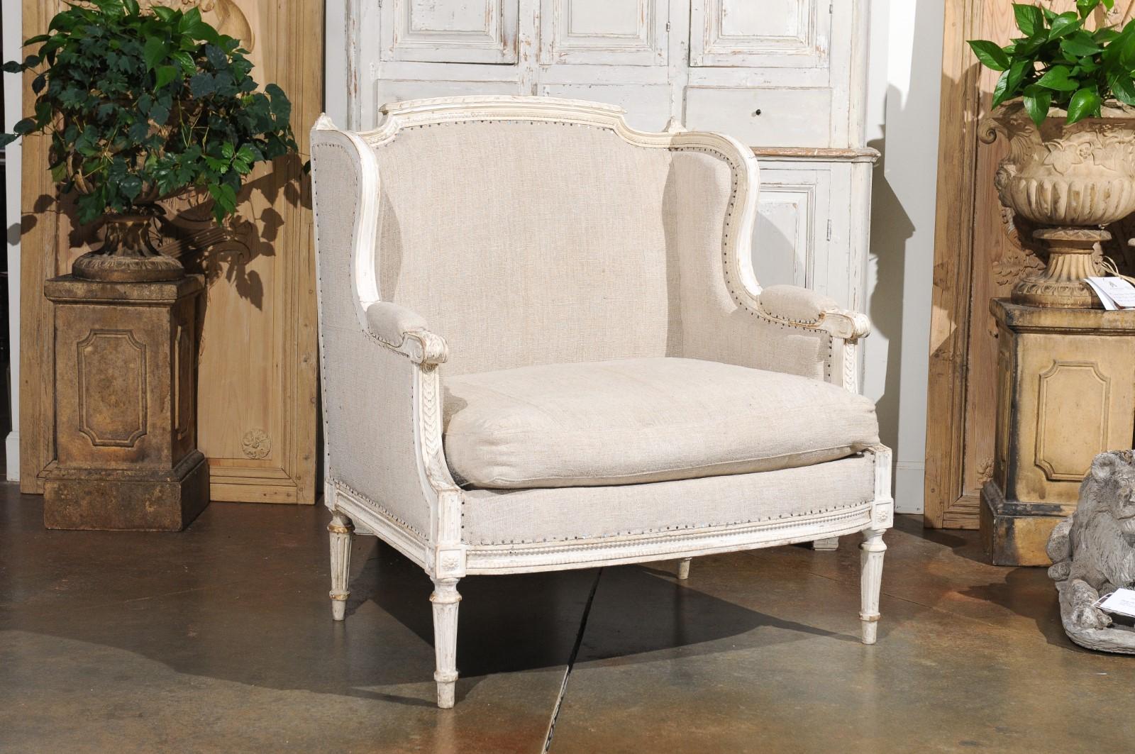 A French Louis XVI style painted and carved wood marquise wingback chair from the 20th century, with new upholstery. Created in France during the 20th century, this marquise chair features a straight back, topped with a carved upper rail flanked