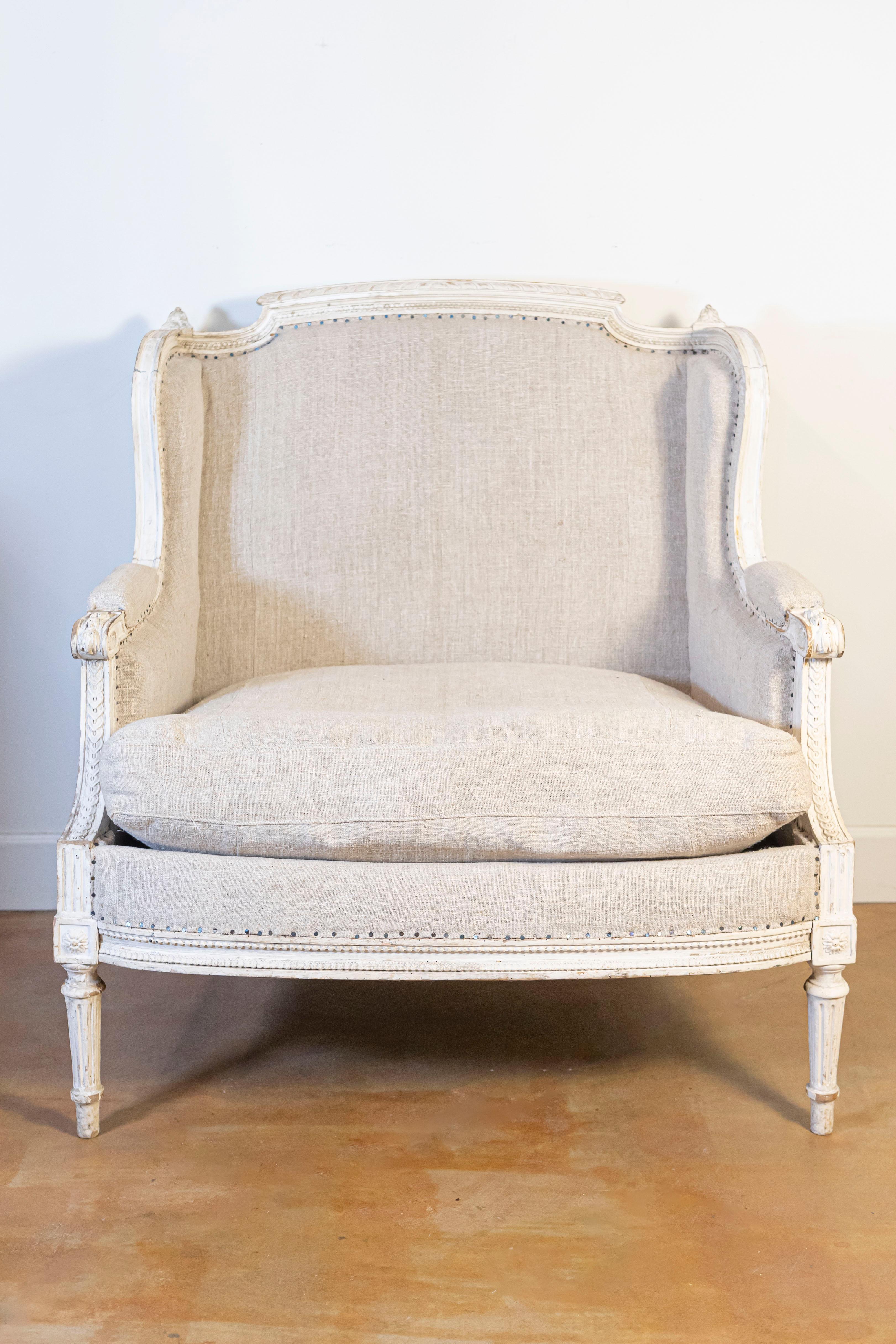 A French Louis XVI style painted and carved wood marquise wingback chair from the 20th century, with new upholstery. Created in France during the 20th century, this marquise chair features a straight back, topped with a carved upper rail flanked