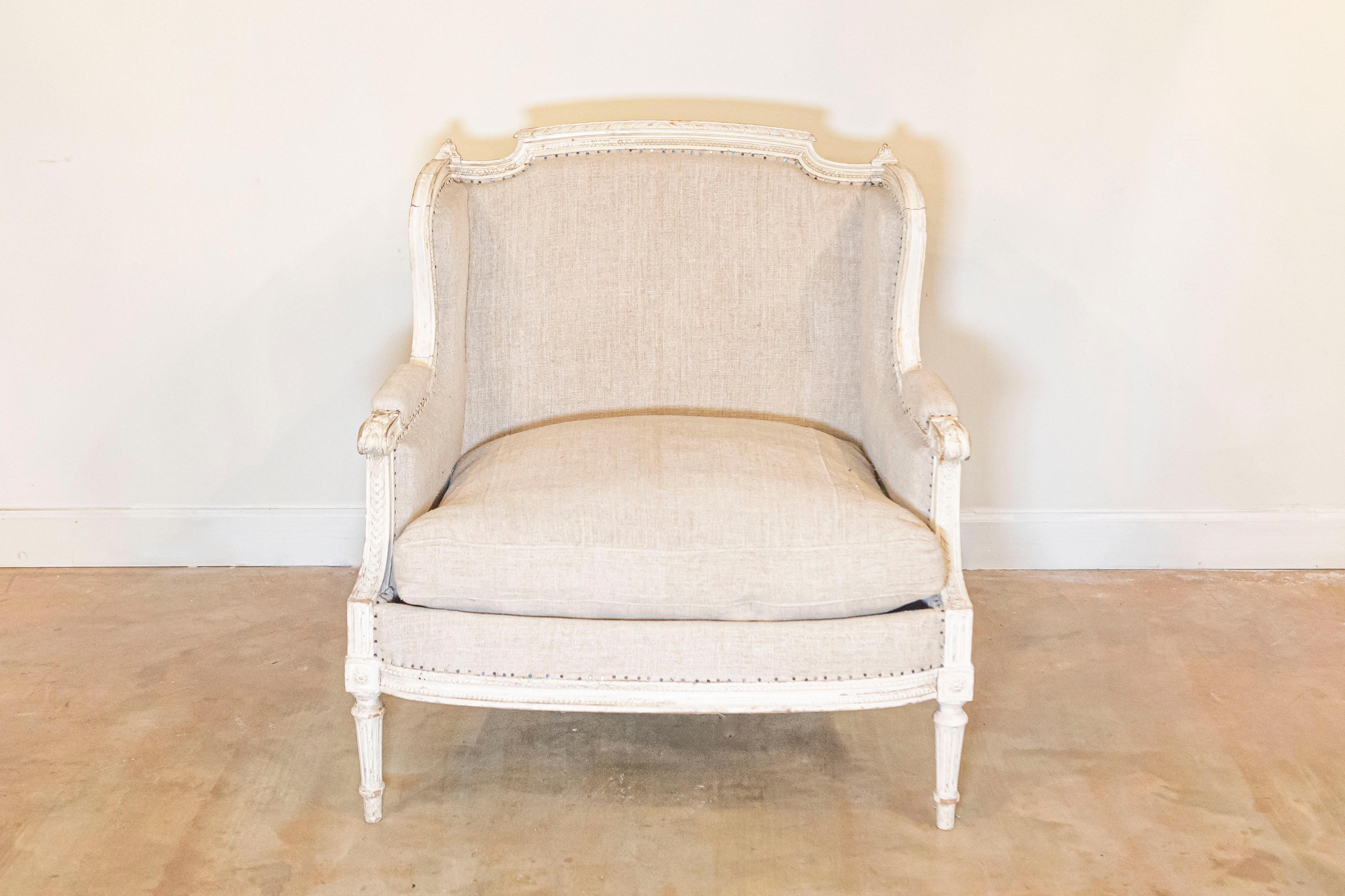 A French Louis XVI style painted and carved wood marquise wingback chair from the 20th century, with new upholstery. Created in France during the 20th century, this marquise chair features a straight back, topped with a carved upper rail flanked