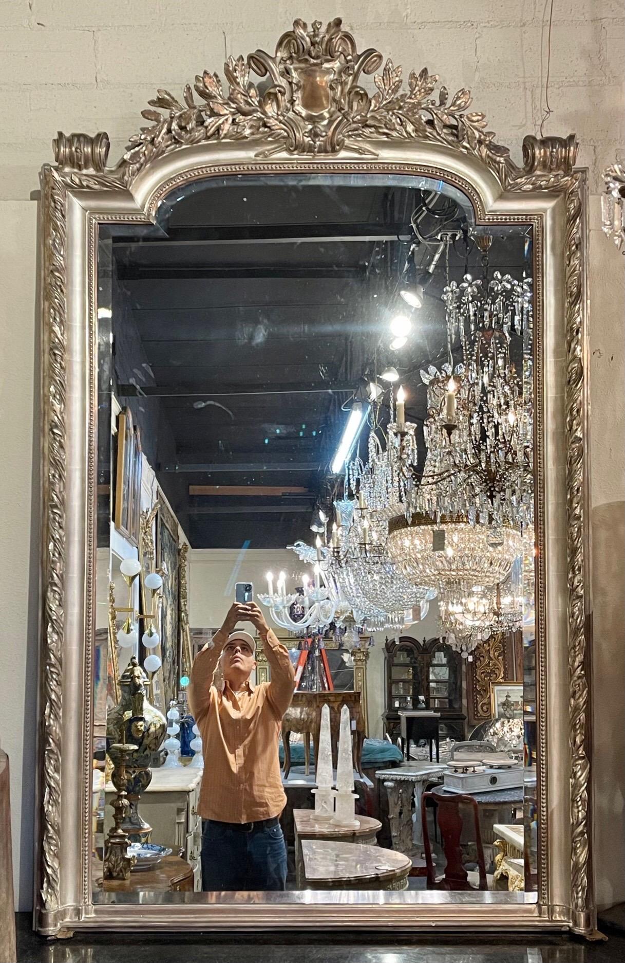 Amazing large scale French Louis XVI style carved and silver leaf mirror with beveled glass. Featuring an elaborately carved crest at the top of the mirror and a fabulous finish. Stunning!