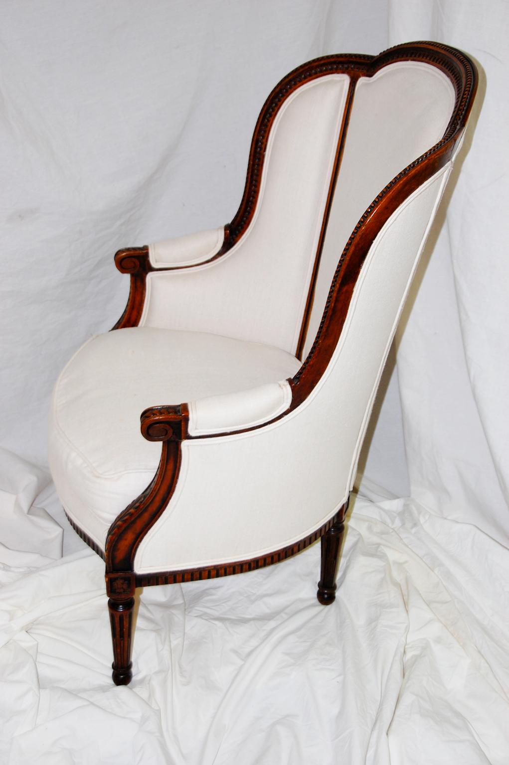 French Louis XVI style carved beechwood bergère chair in cream colored linen. The frame is crisply carved with acanthus leaf and running beads with carved stop fluted tapered turned legs. The division of the upholstery into three sections in both