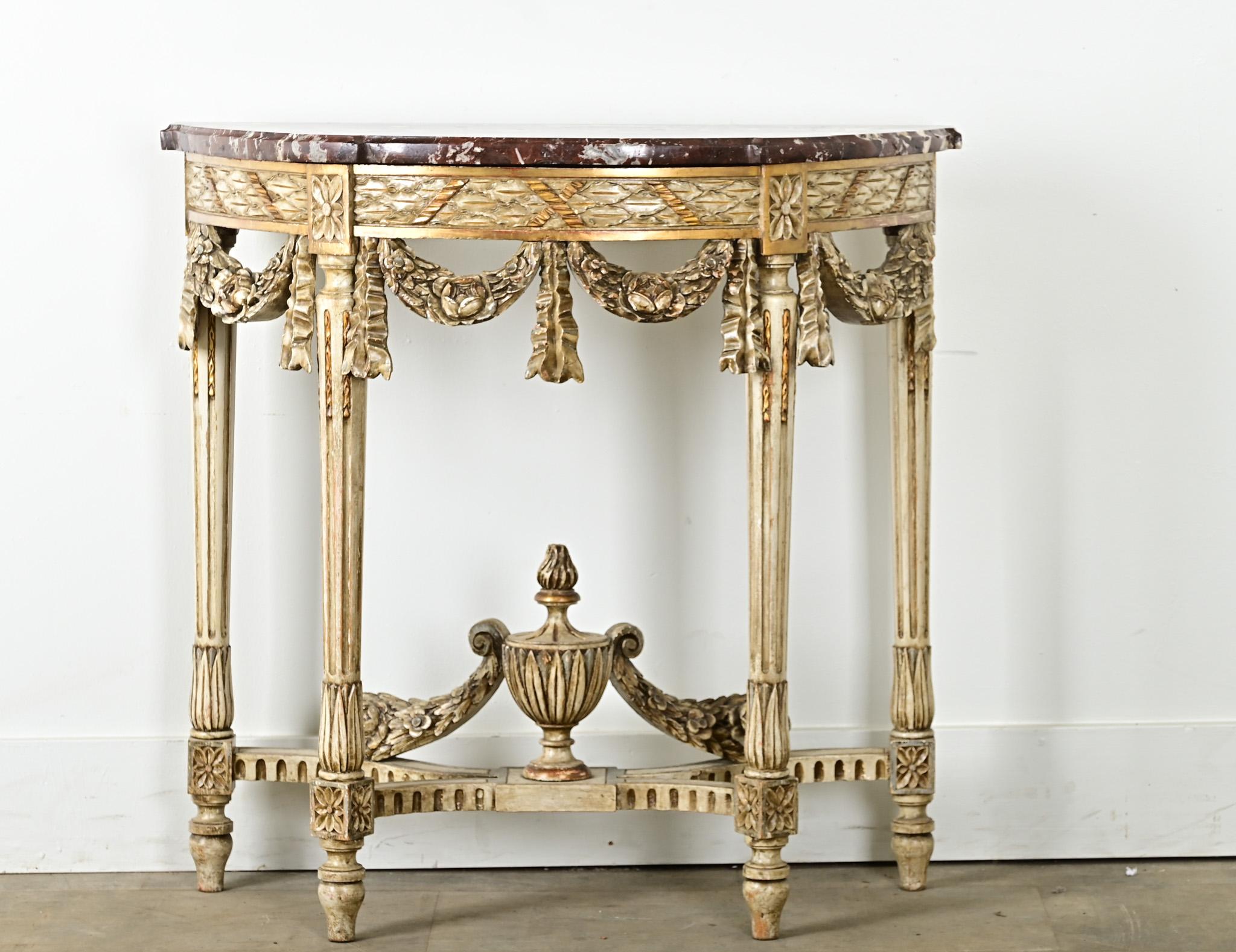A petite French Louis XVI style demilune console from the 1800’s. This impressive little console has its original hand cut marble top shaped to fit its base. The painted wood base is made of many carved decorative motifs from the Louis XVI style