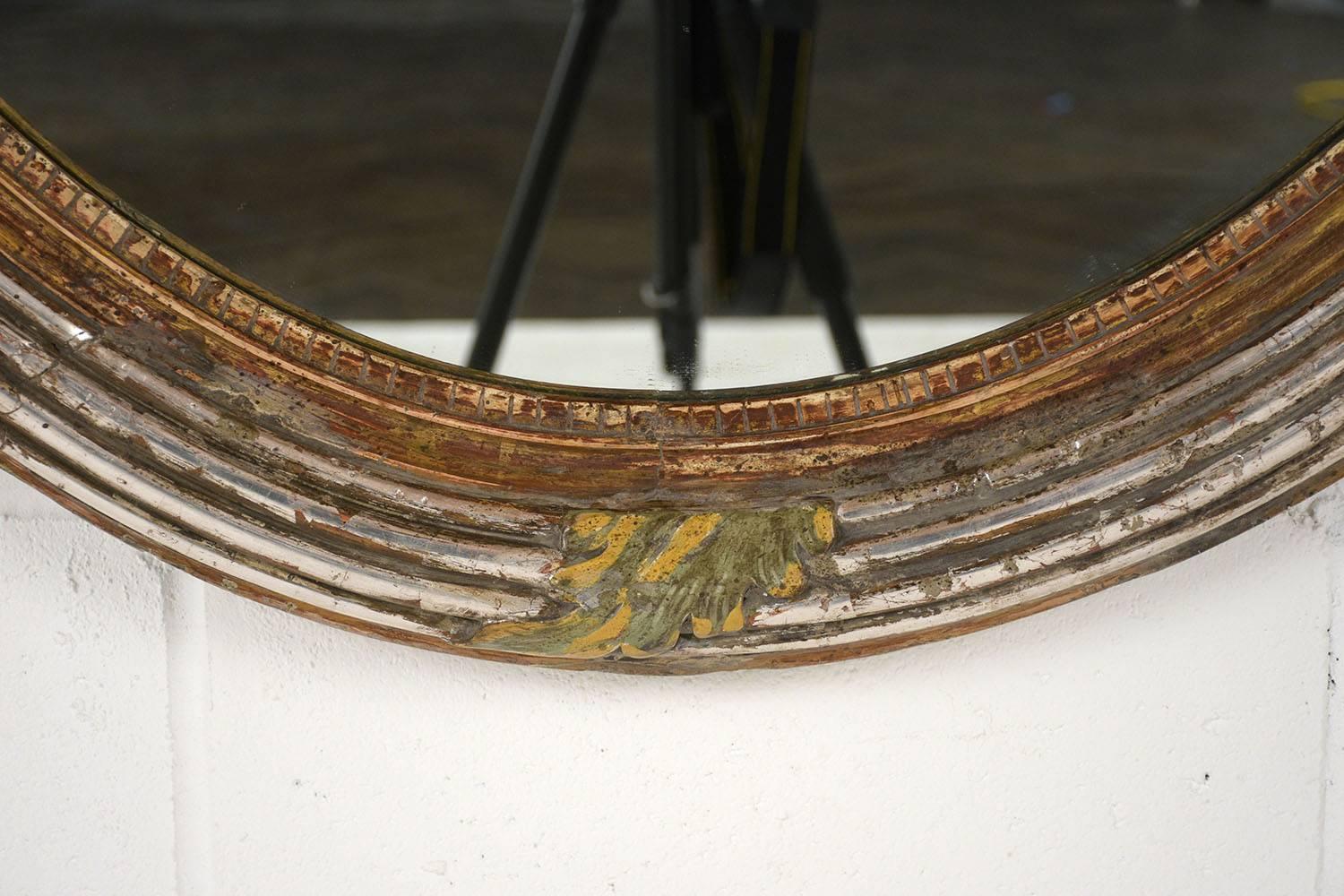 This Late 19th Century French Louis XVI Style Oval Wall Mirror features a stunning handcrafted giltwood frame with carved leafy and fluted details and is in great condition. The frame is adorned with silver leaf & gold leaf accents and has its
