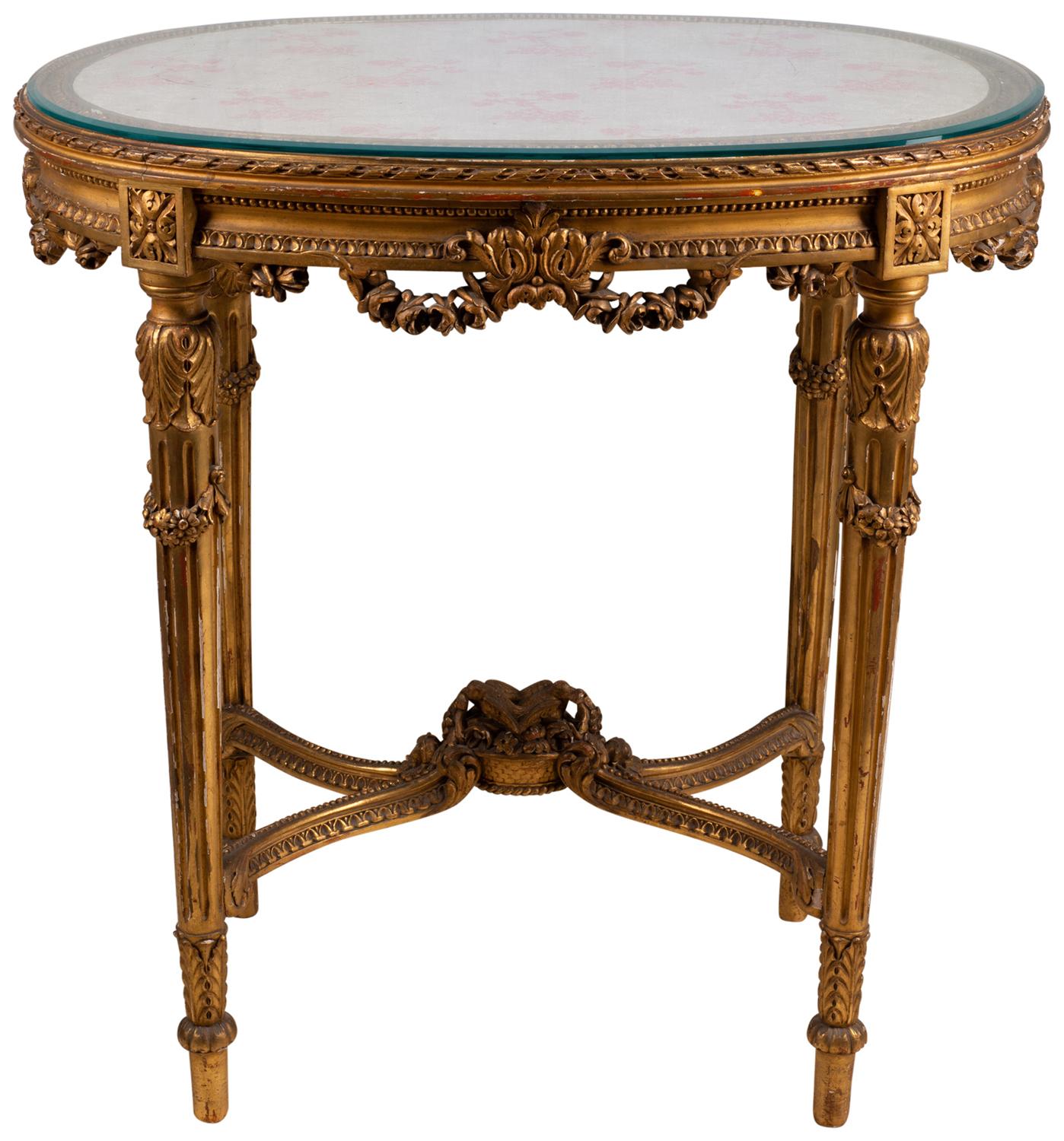 A good quality early 20th century carved giltwood occasional table, having an inset silk panel with glass top. A carved frieze with garlands of flowers, egg and dart molding, raised on turned tapering fluted legs, also with carved floral decoration