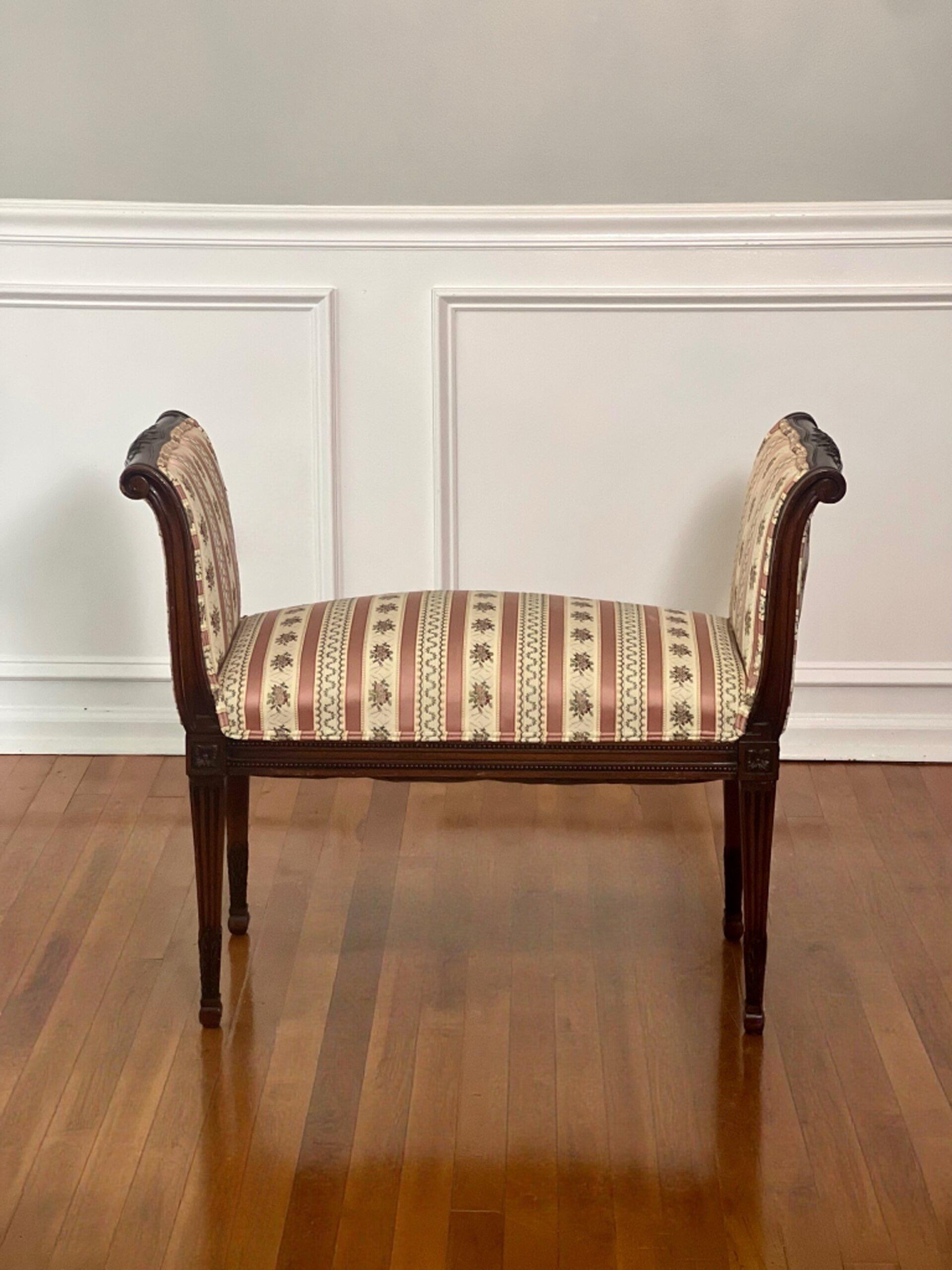 Lovely French Louis XVI style carved mahogany upholstered bench, circa 1920.  Gently scrolled arms feature floral carving on the top with carved detail flowing down to the all-around beaded apron with rosettes on the corners and tapered fluted legs