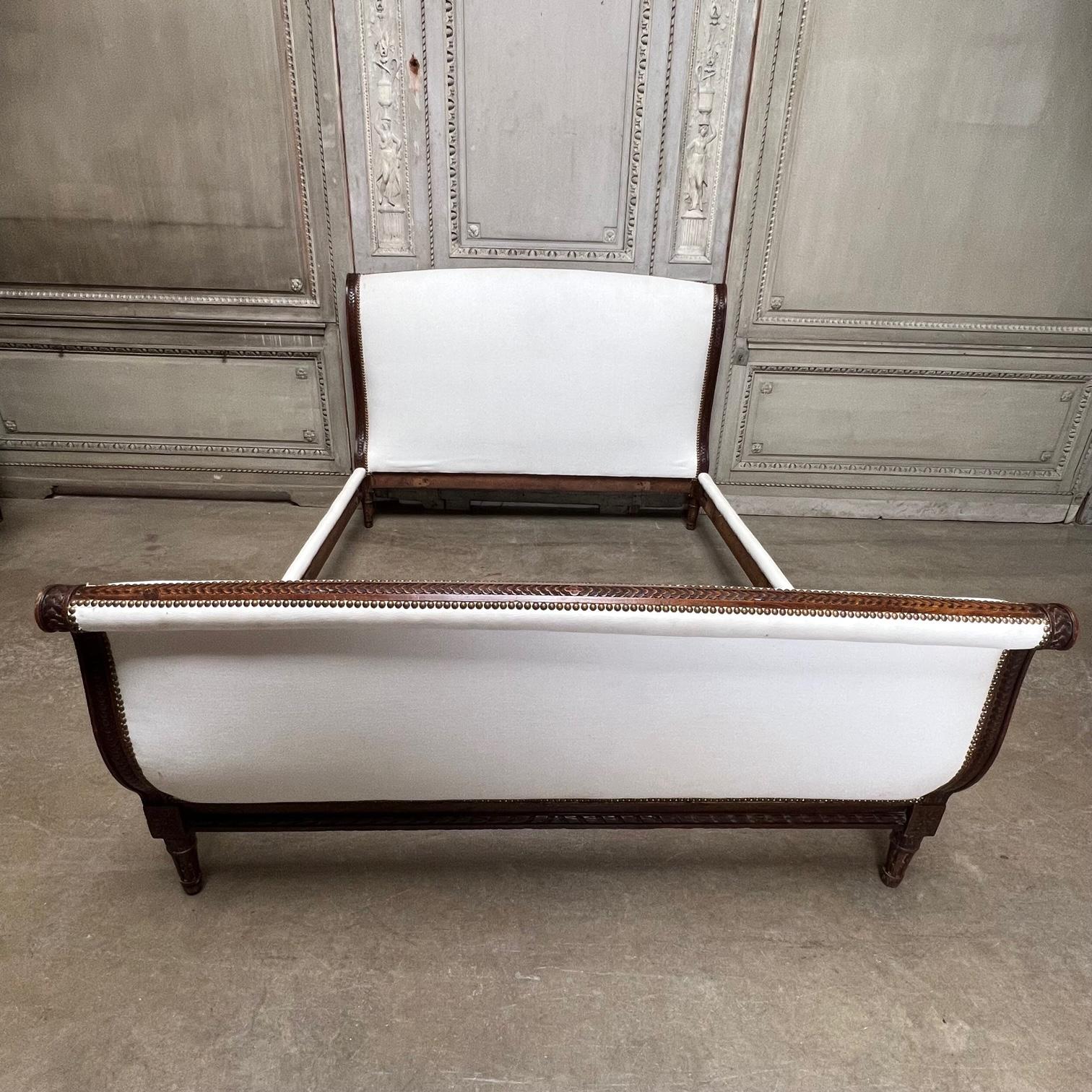 Un lit français de style Louis XVI en bois de hêtre sculpté avec une finition en noyer date du début du XXe siècle. On l'appelle un lit en bateau en français en raison de sa forme, qui s'incurve à la fois de la tête de lit et du pied de lit. Il est
