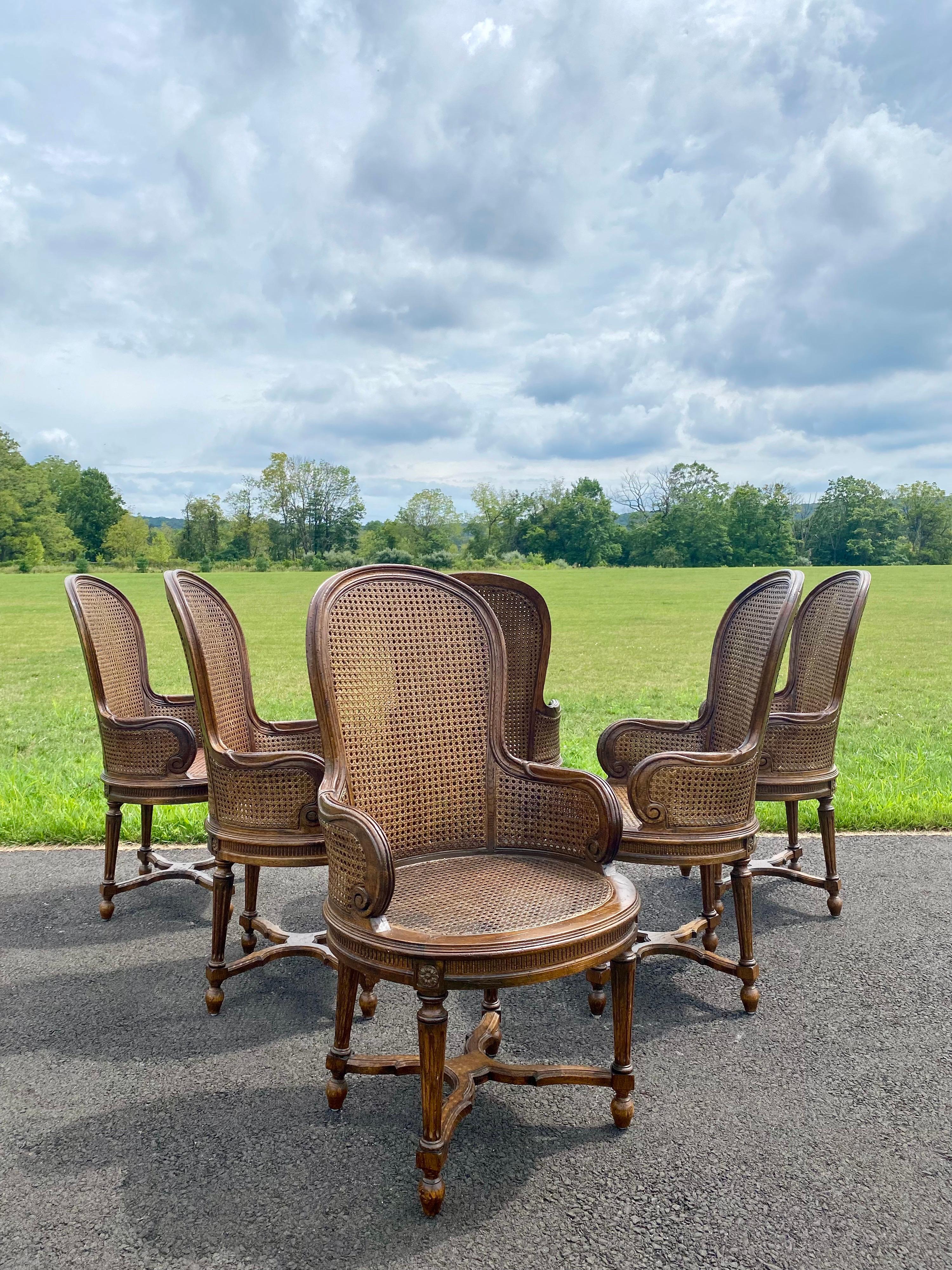 Set of six perfectly proportioned balloon shaped stained wood dining arm chairs with single caned seats and double caned backs. These French Louis XVI style chairs feature beautifully curved backs and arms with medallion carved details, fluted legs,