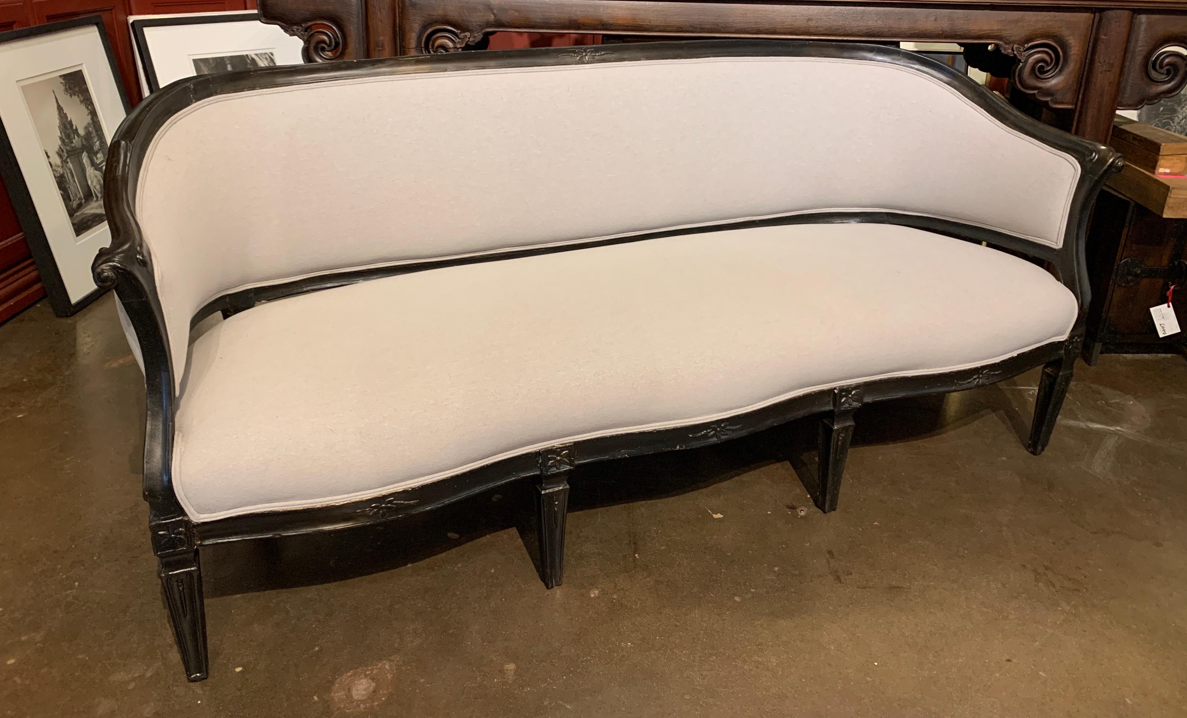 A simple and elegant carved and ebonized wood and upholstered sofa, known as a 