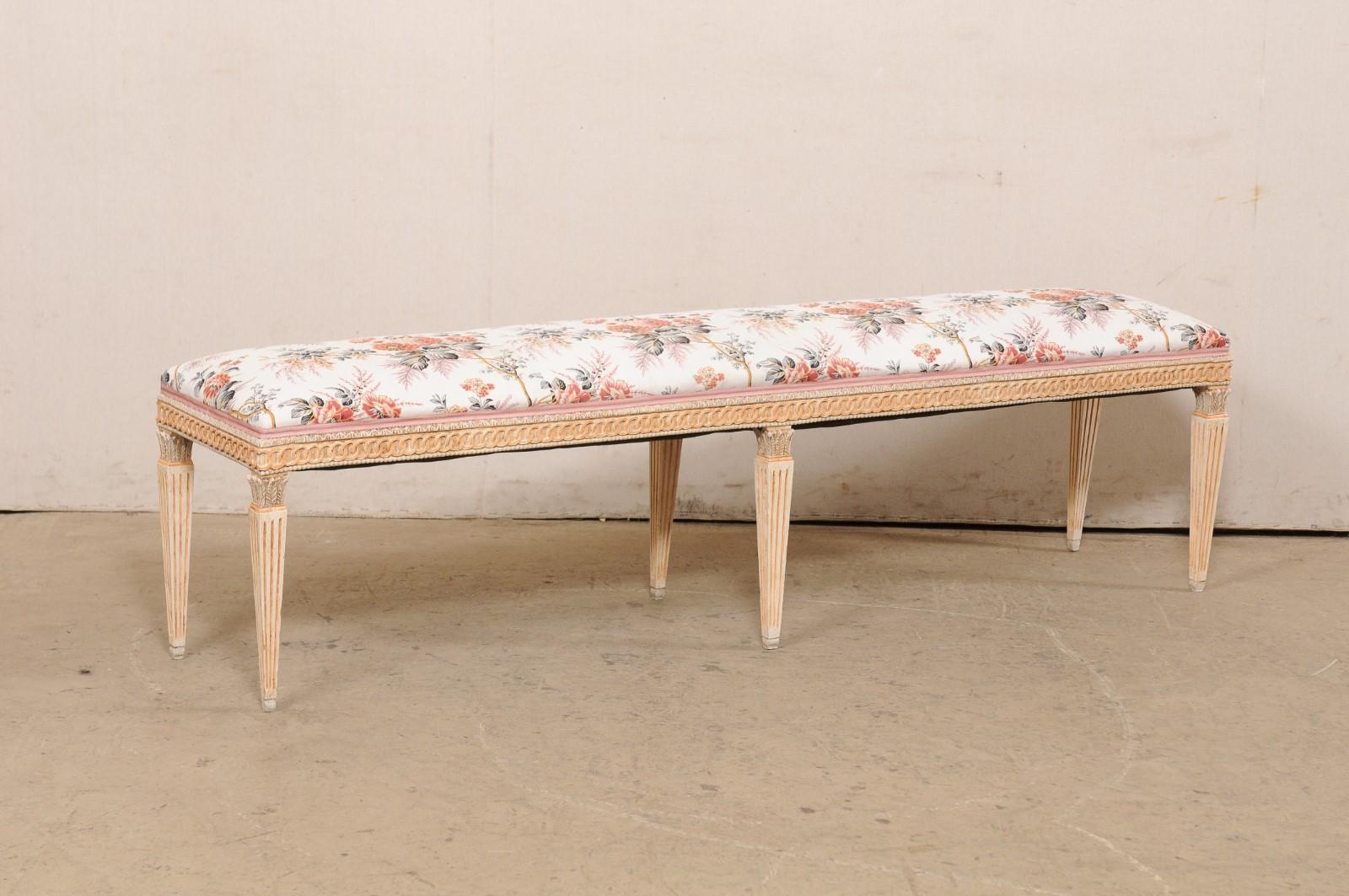 A French Louis XVI style carved-wood bench with its original finish and floral upholstered seat. This vintage bench from France has been nicely carved on all sides, with a circular linked chain and beaded trim about the apron, and presented upon six