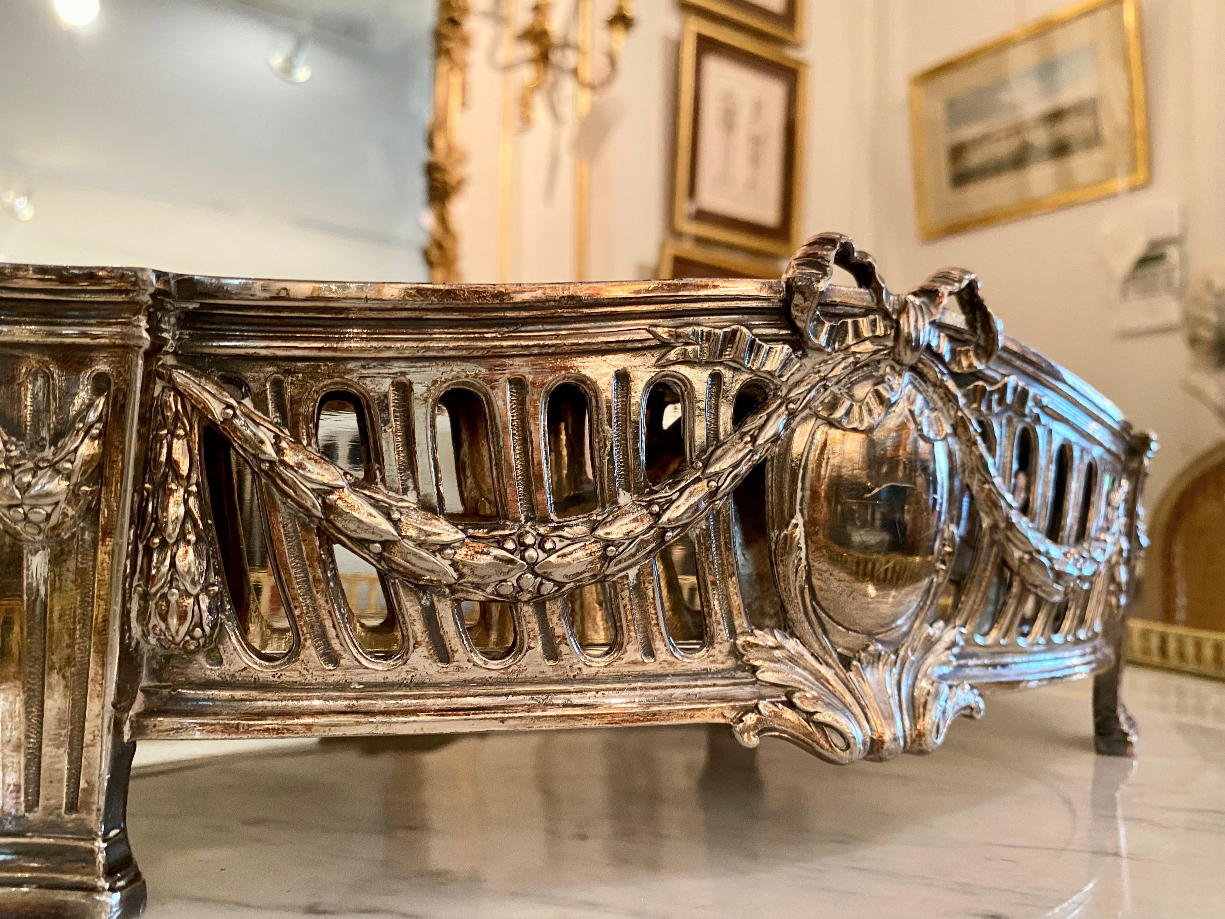 An elegant French 19th century Louis XVI style silvered bronze centerpiece with metal removable insert. The centerpiece is raised on columned feet and adorned in the neoclassical, Louis XVI vernacular, with swags, garlands and bows surrounding an