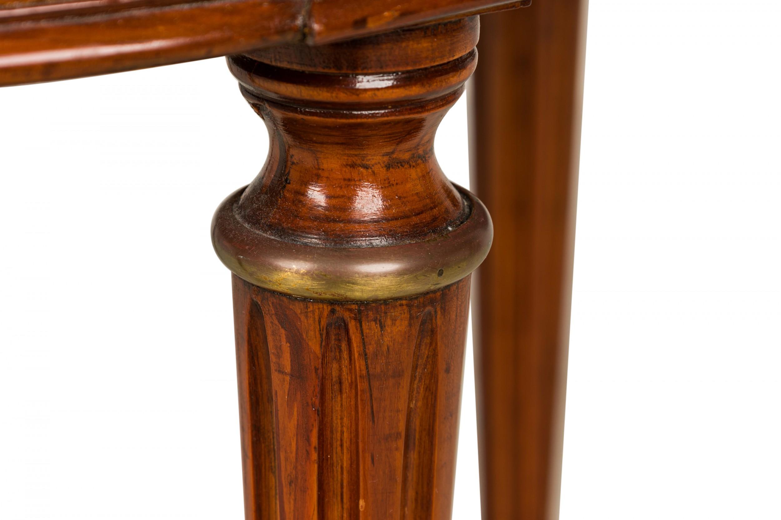 Mesa bouillotte circular de caoba, estilo Luis XVI francés (2ª mitad del siglo XIX), con tablero de mármol negro con galería de filigrana de bronce sobre dos cajones con tiradores de bronce en forma de mano y dos estantes laterales de cuero repujado