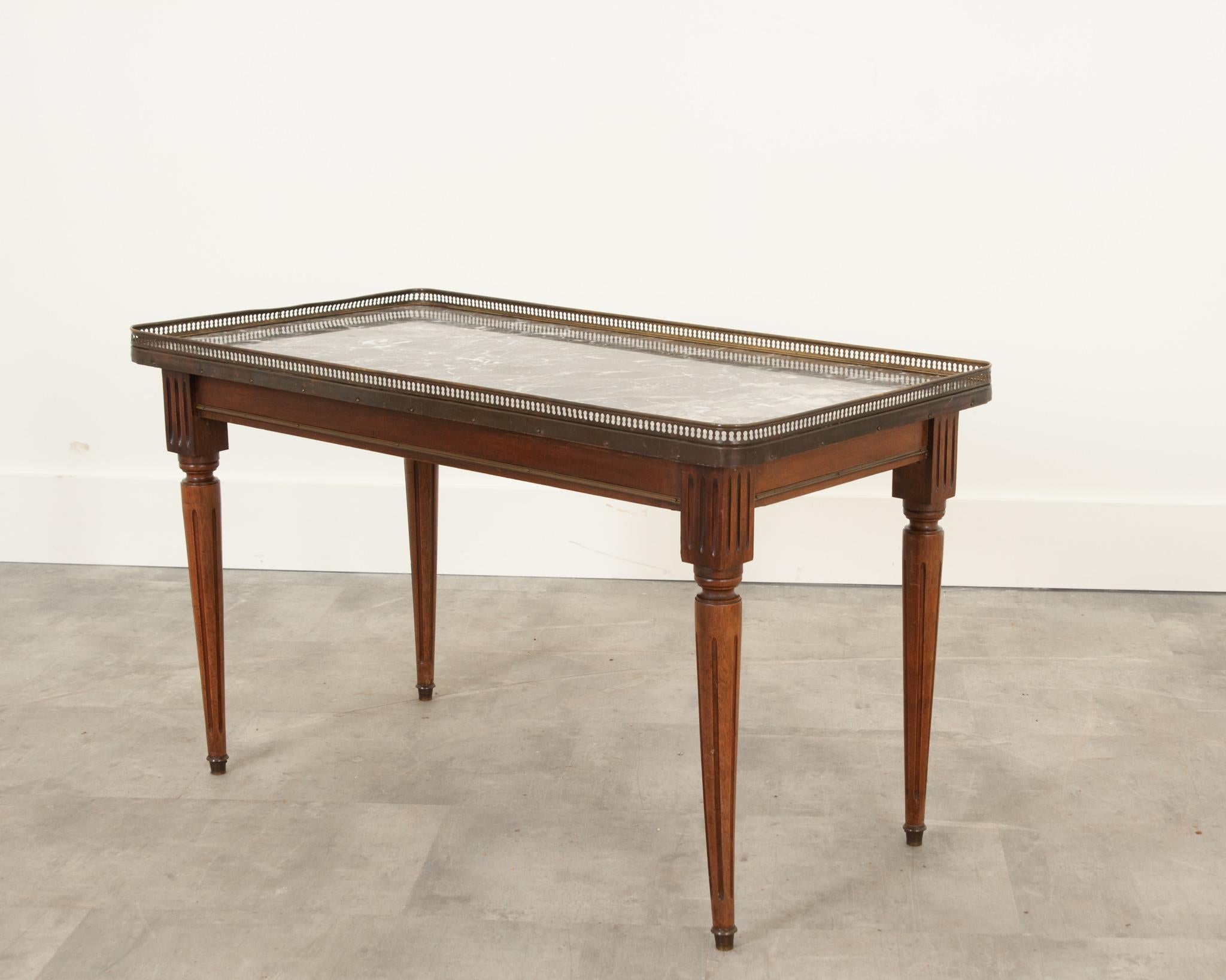 French coffee table in the Louis XVI style. A simple pierced brass gallery surrounds the inset charcoal & white marble top which has been repaired, please be sure to view the detailed images. The base is made of mahogany with brass accents. Great