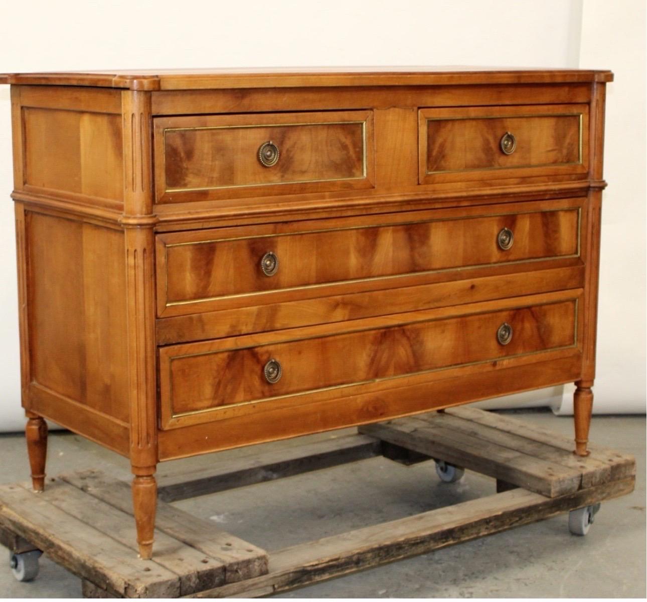 French Louis XVI style Walnut commode with a bronze trim. 
This commode features fluted side posts and tapered legs. Its brass hardware evokes a neoclassical style. 

31 1/4