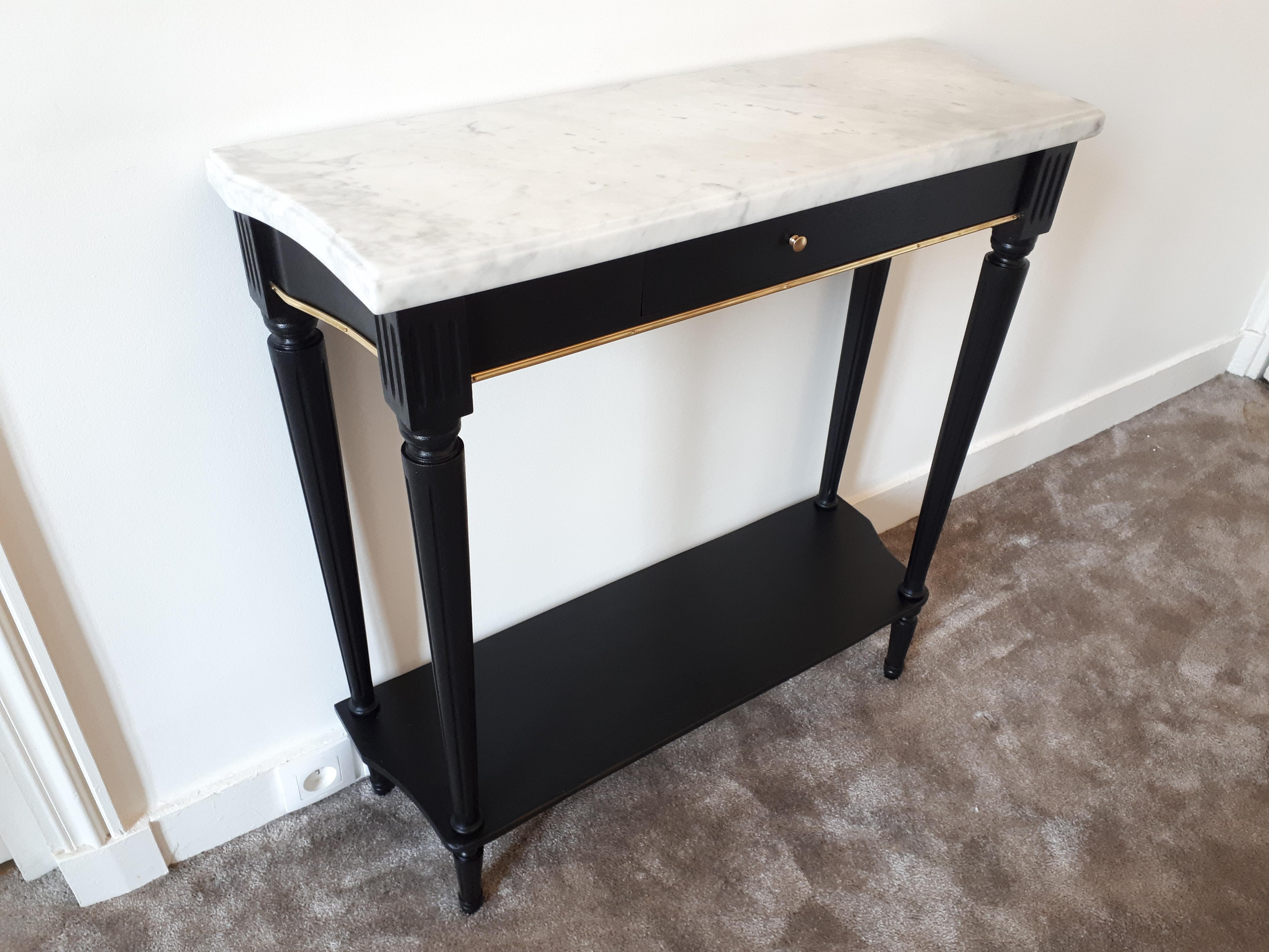 French Louis XVI style console with a dovetail drawer in front and top is in Carrara marble 3 centimeters thick. 
The legs and feet are fluted and meet by a lower shelf. 
This piece is mahogany painted black. 
Golden brass chopsticks highlight